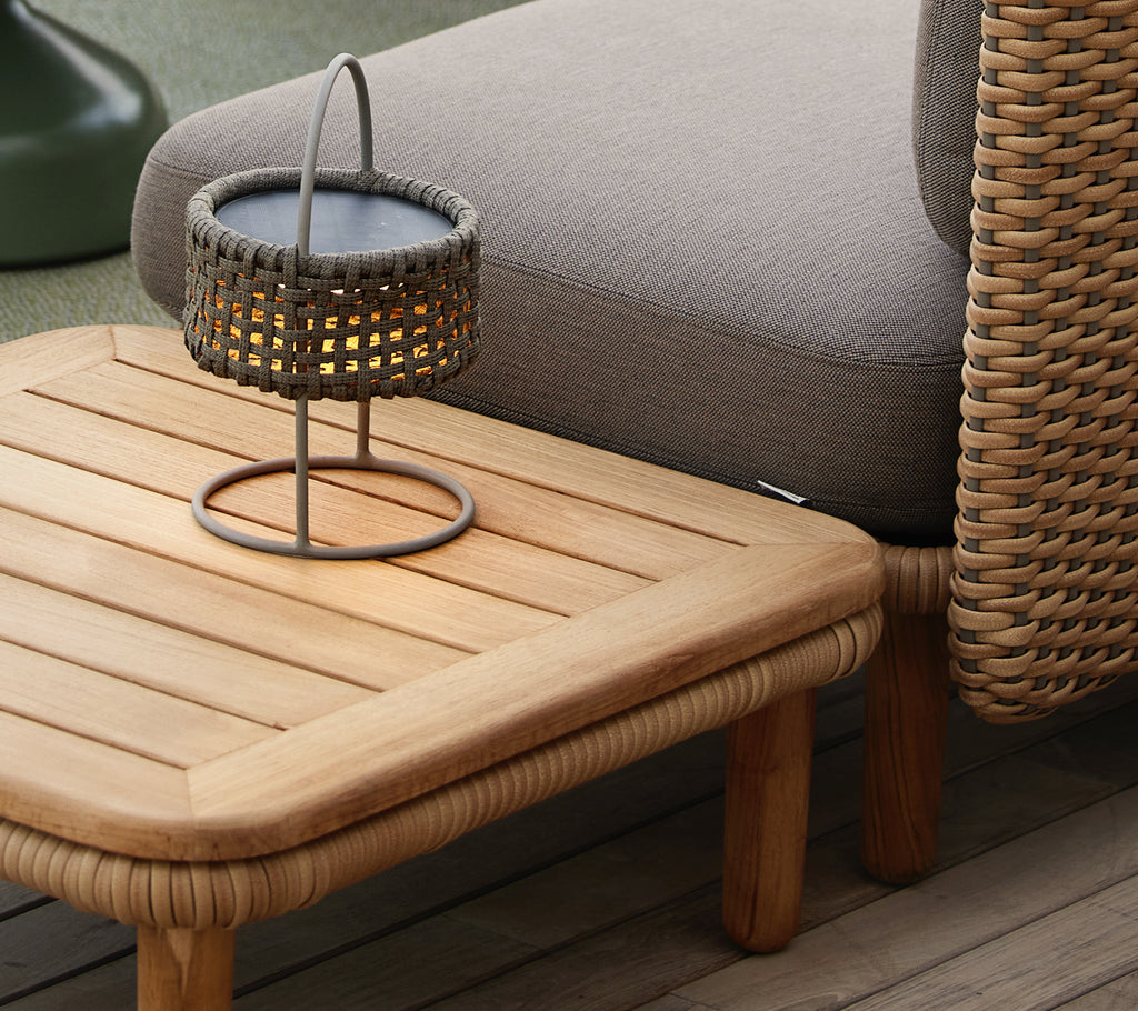 Teak coffee table with a slatted top, accompanied by a woven lamp, creating a cozy and inviting atmosphere.