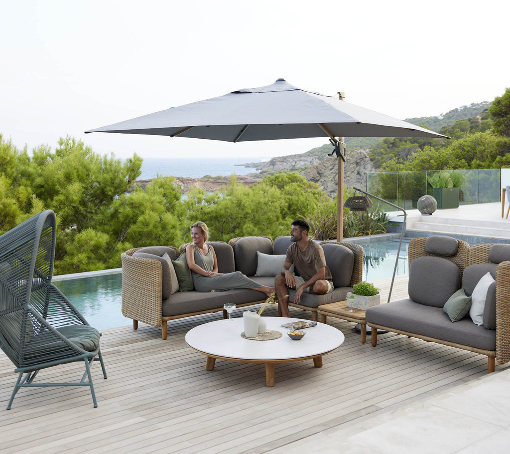 A stylish lounge area featuring comfortable seating, a large umbrella, and a round table, surrounded by greenery and a serene view.