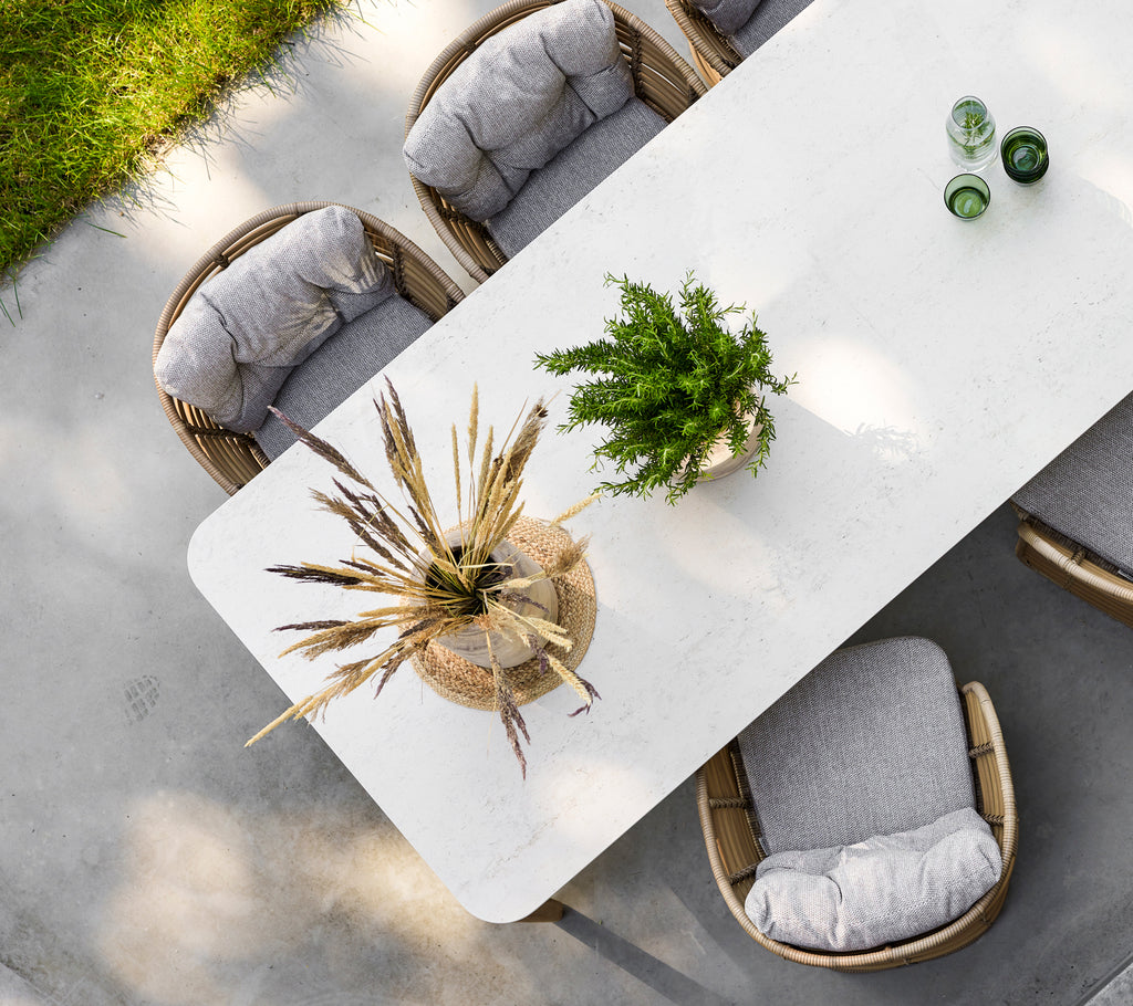 A modern dining table with a textured surface, surrounded by cushioned chairs and adorned with a stylish plant centerpiece.