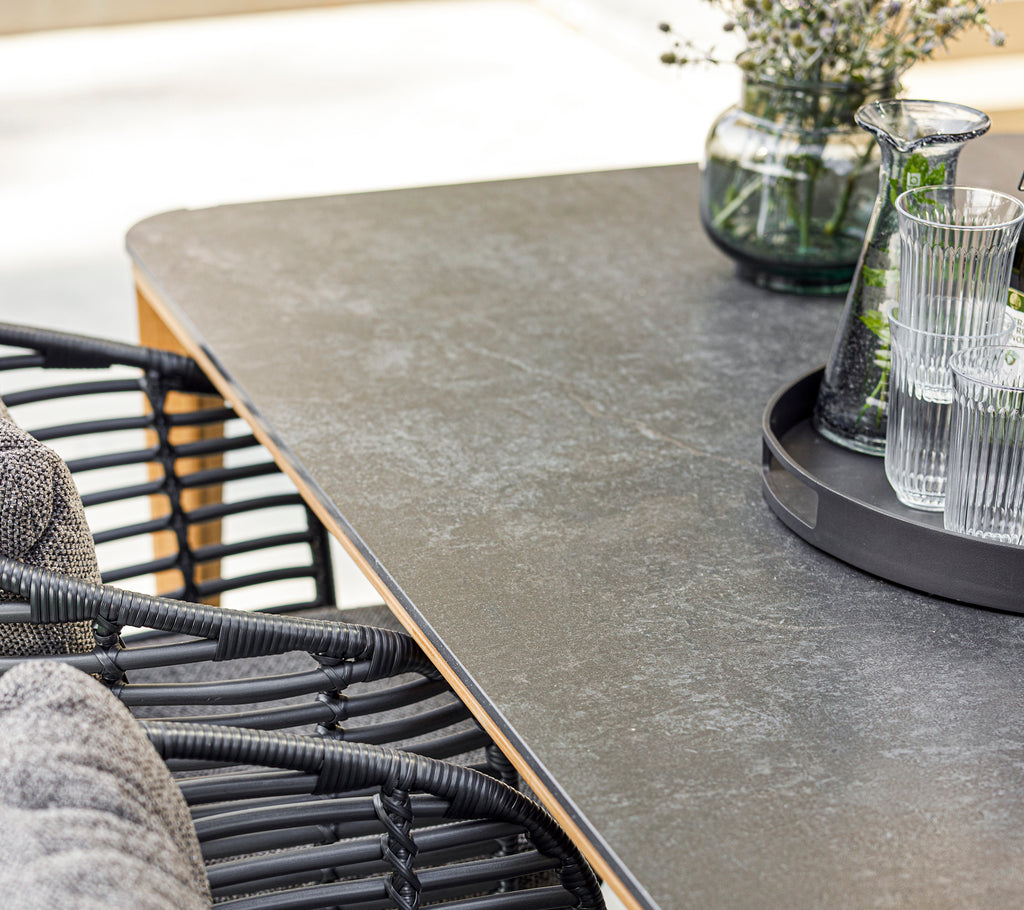A modern dining setup featuring a smooth tabletop, stylish basket chair, glassware on a tray, and a decorative vase with greenery.