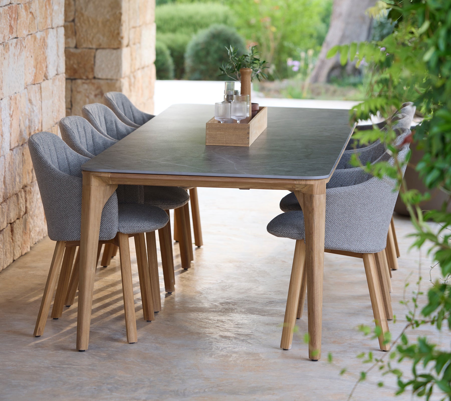 Modern dining table set with grey chairs in a natural outdoor setting.
