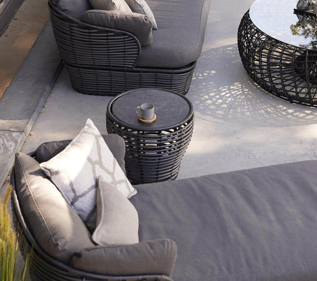 A small graphite basket coffee table beside a modern lounge chair with cushions, enhancing a stylish seating area.