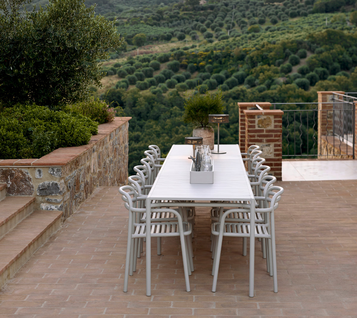 A stylish seating arrangement featuring Bliss chairs and table in sand color, complemented by an Illusion lamp, set against a lush landscape.