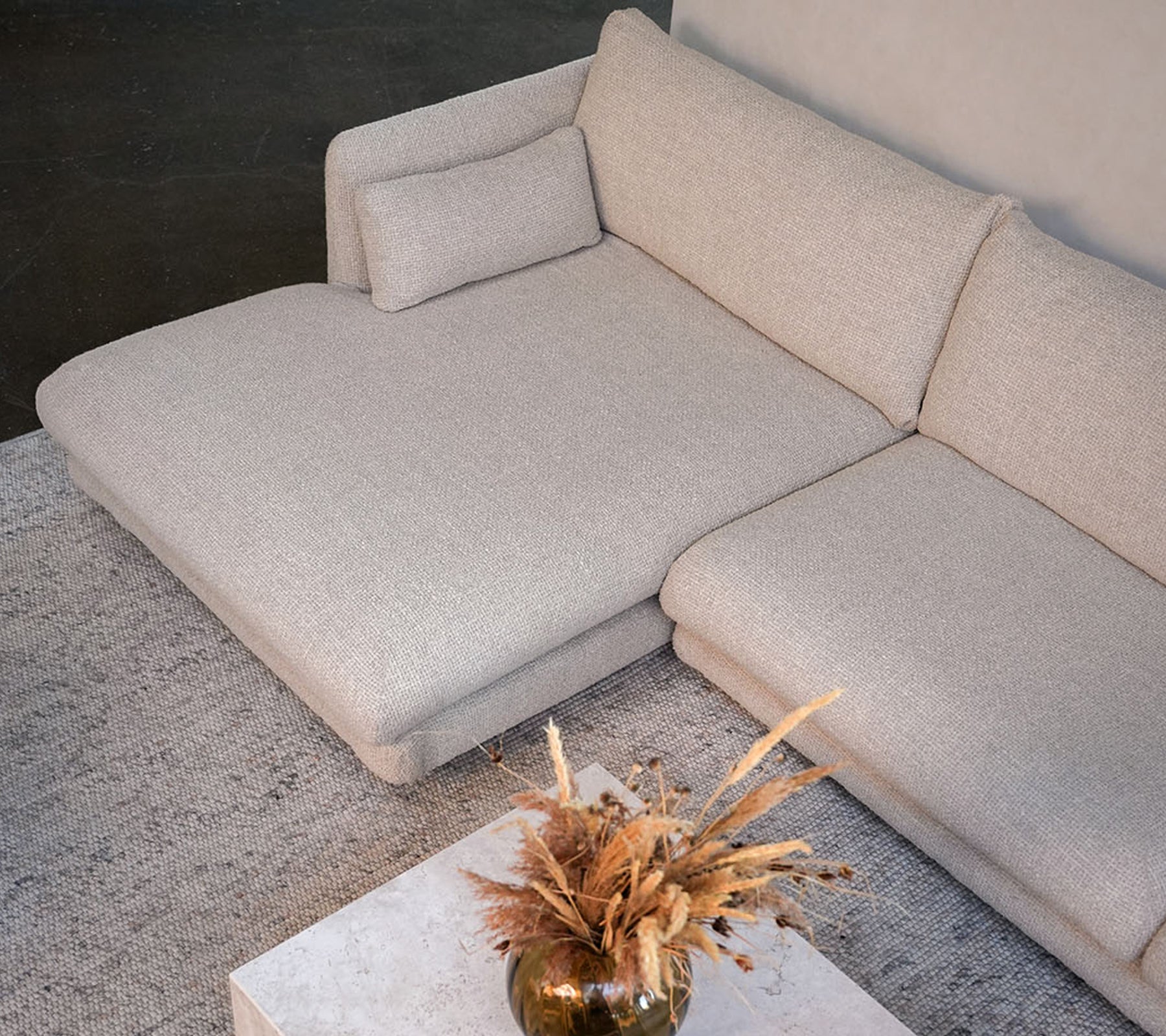 Modern beige sofa with a white table and decorative vase in a stylish lounge setting.
