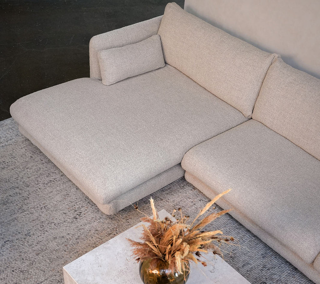 Modern beige sofa with a white table and decorative vase in a stylish lounge setting.