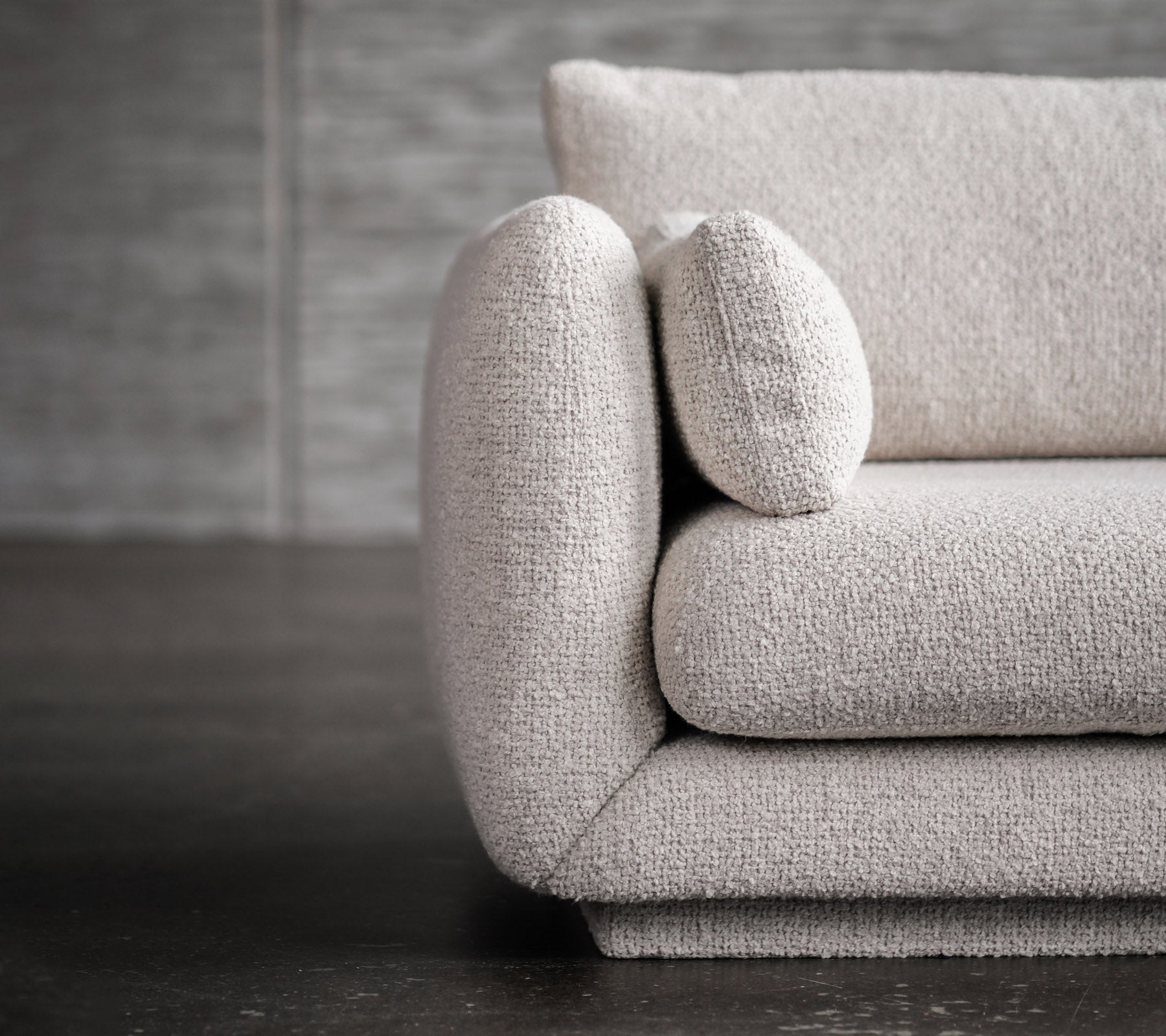 Modern light grey sofa with rounded arm and cushion detail.