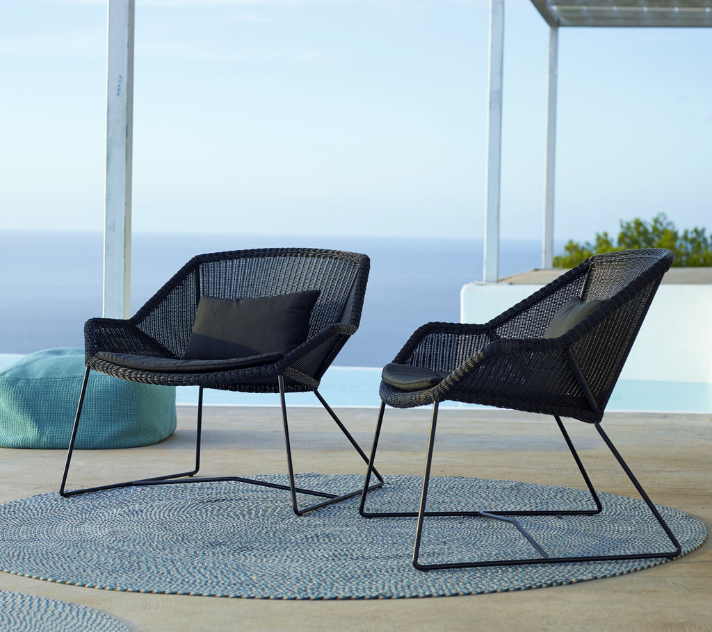 Two modern black chairs with a blue cushion on a round rug by the pool.