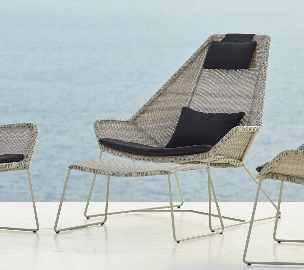Modern woven chair with a black cushion by the water.