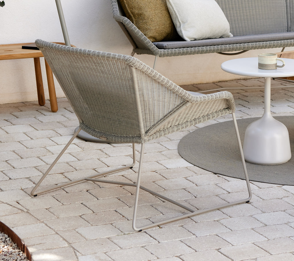 Grey lounge chair with white side table in a modern outdoor setting.