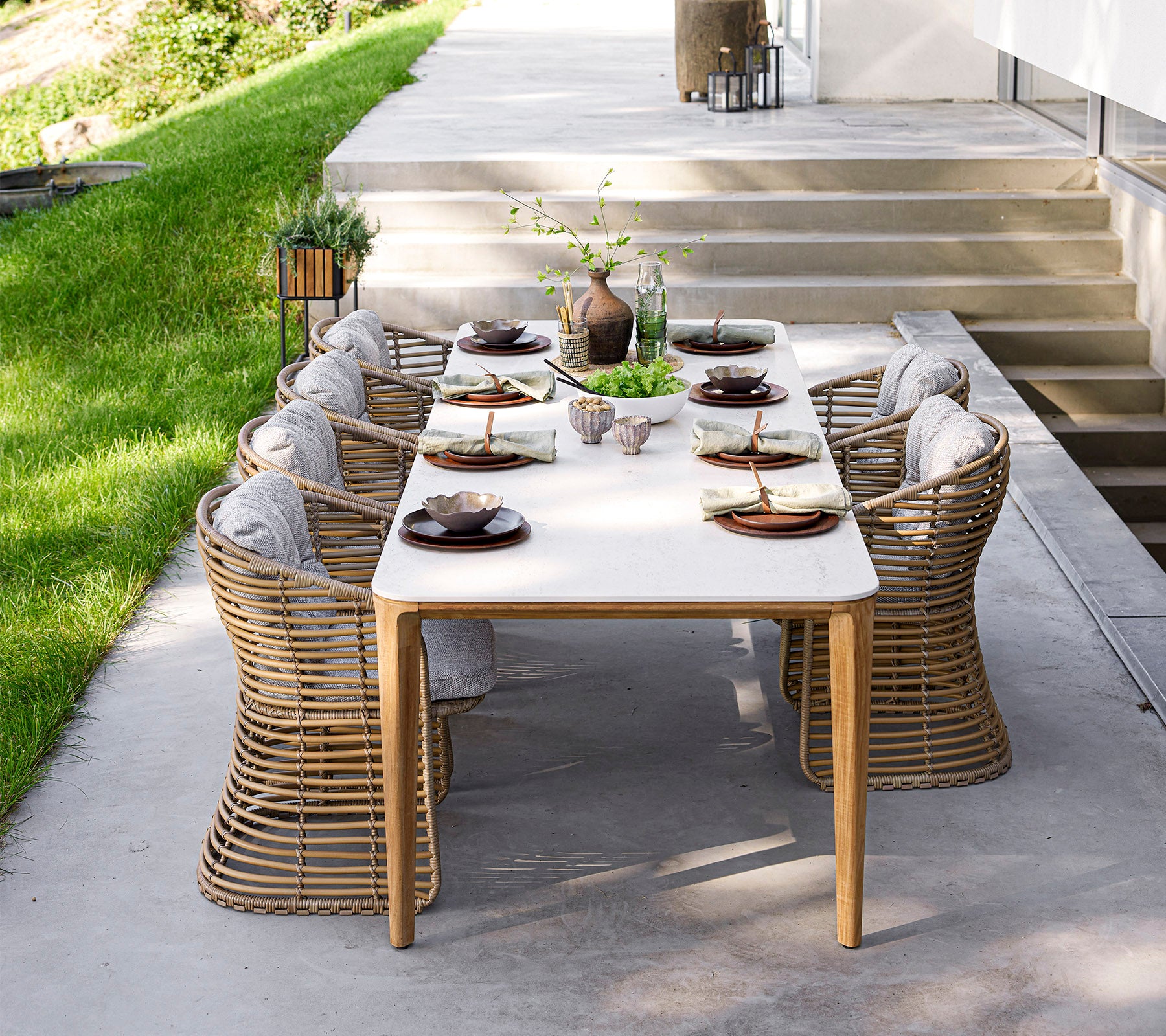 A stylish dining table set with elegant tableware and comfortable chairs, surrounded by greenery and natural light. Perfect for gatherings.