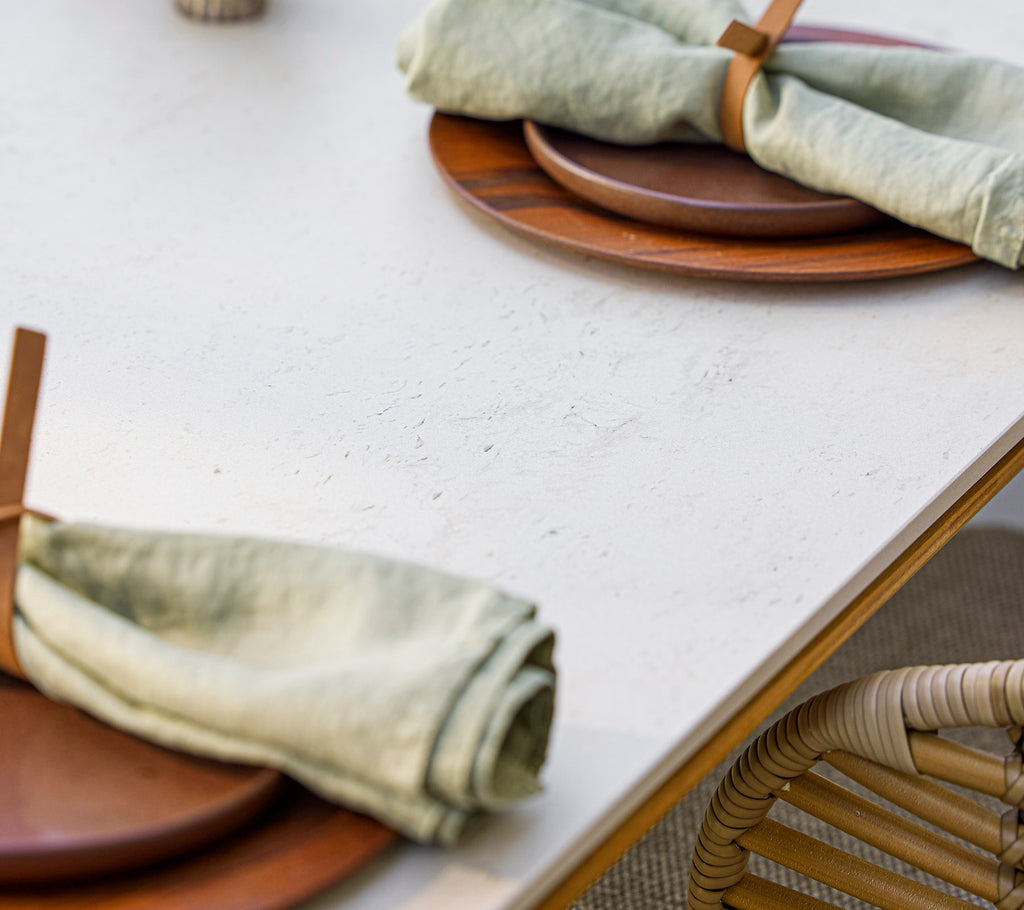 Table setting with wooden plates and elegantly rolled green napkins secured with a wooden holder, creating a natural and inviting atmosphere.