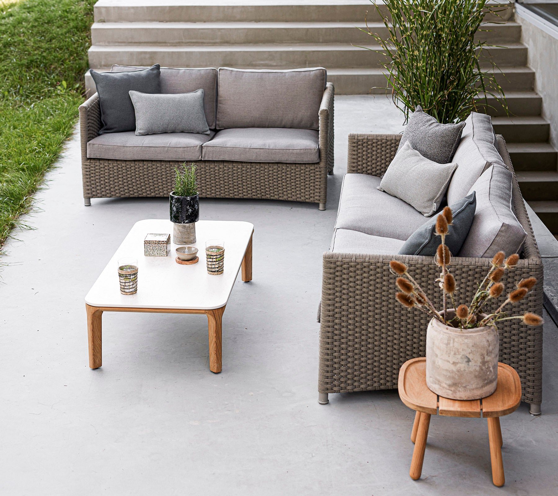 Stylish outdoor seating arrangement featuring a gray sofa set, a wooden table, decorative vases, and potted plants. Ideal for relaxation.