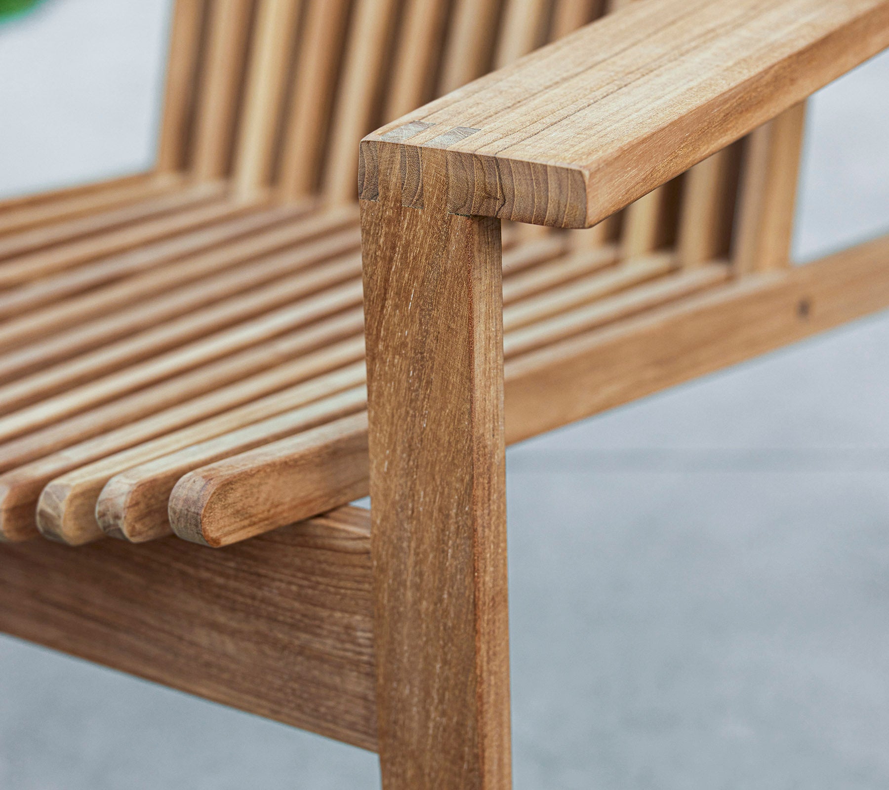 Close-up of a wooden bench with a slatted design and a sturdy armrest, showcasing natural wood grain and craftsmanship.