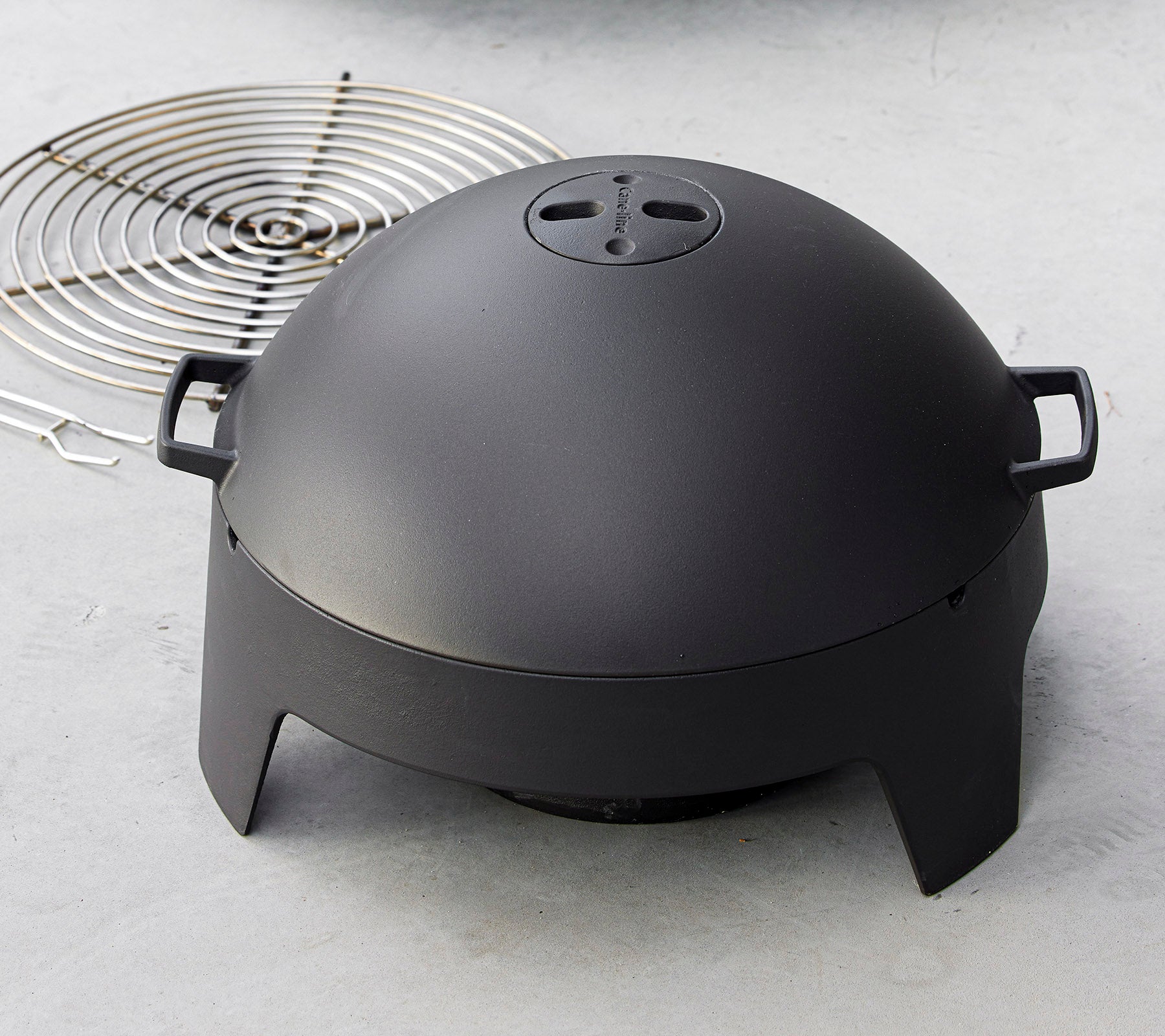 A sleek black cooking appliance with a dome shape and handles, accompanied by a circular grill rack. Ideal for grilling and outdoor cooking.