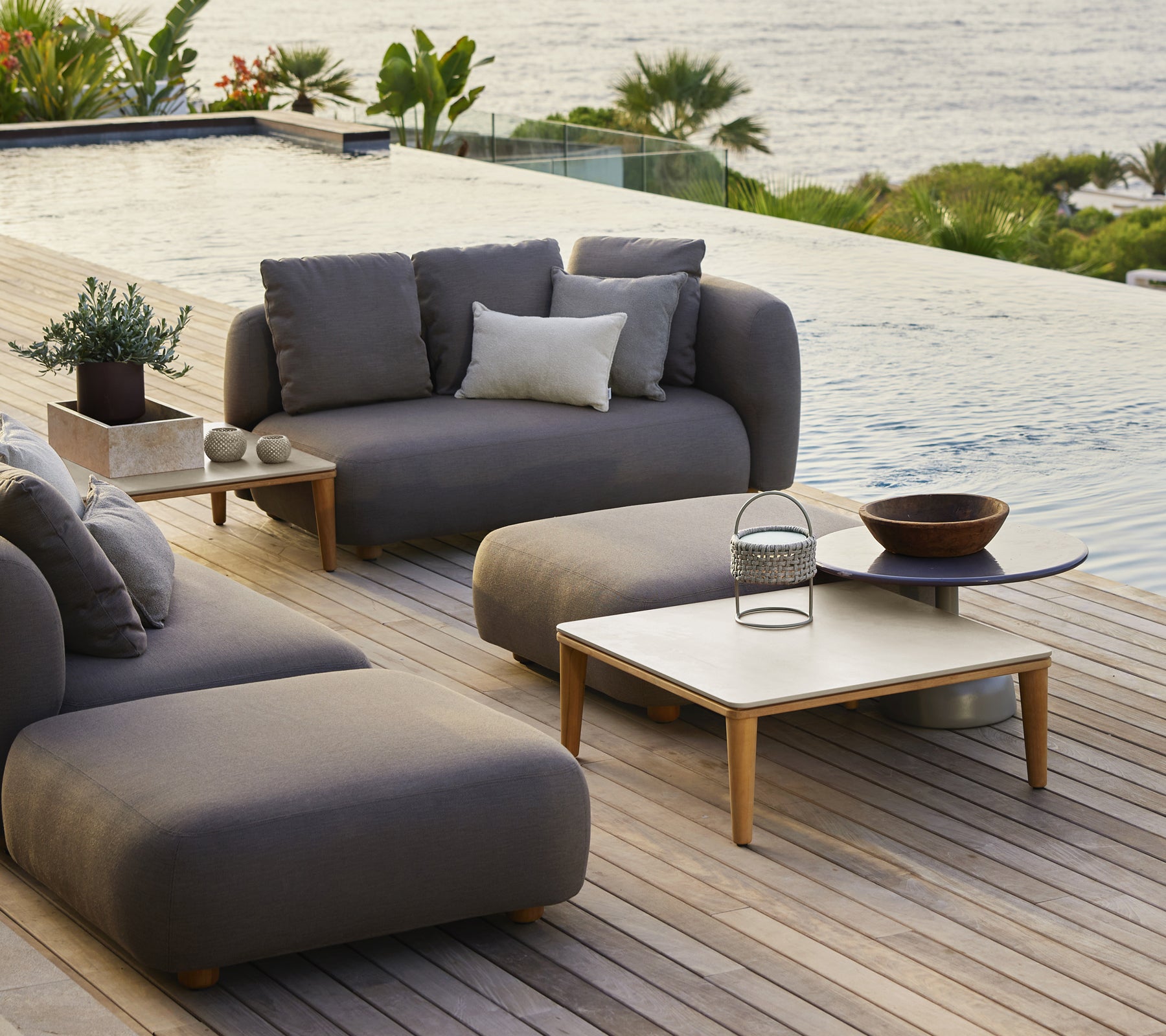 Modern outdoor lounge furniture featuring grey sofa, chair, and wooden coffee table.