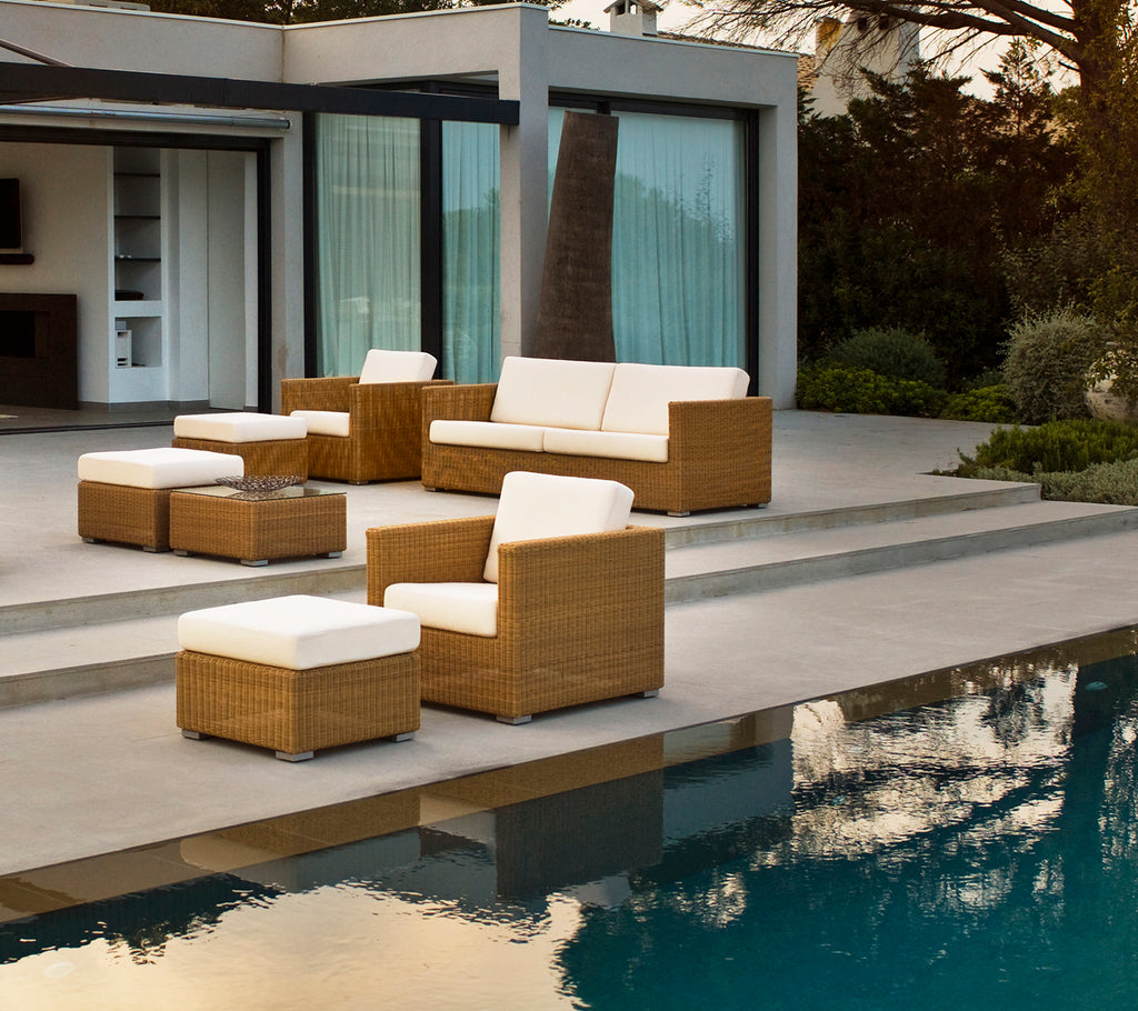 Modern outdoor lounge area with brown sofa, chairs, and cushions by a pool.