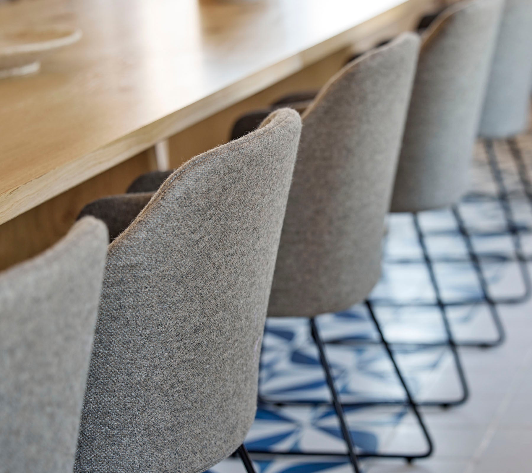 A row of stylish, upholstered chairs with slender metal legs positioned around a wooden table, featuring patterned flooring beneath.