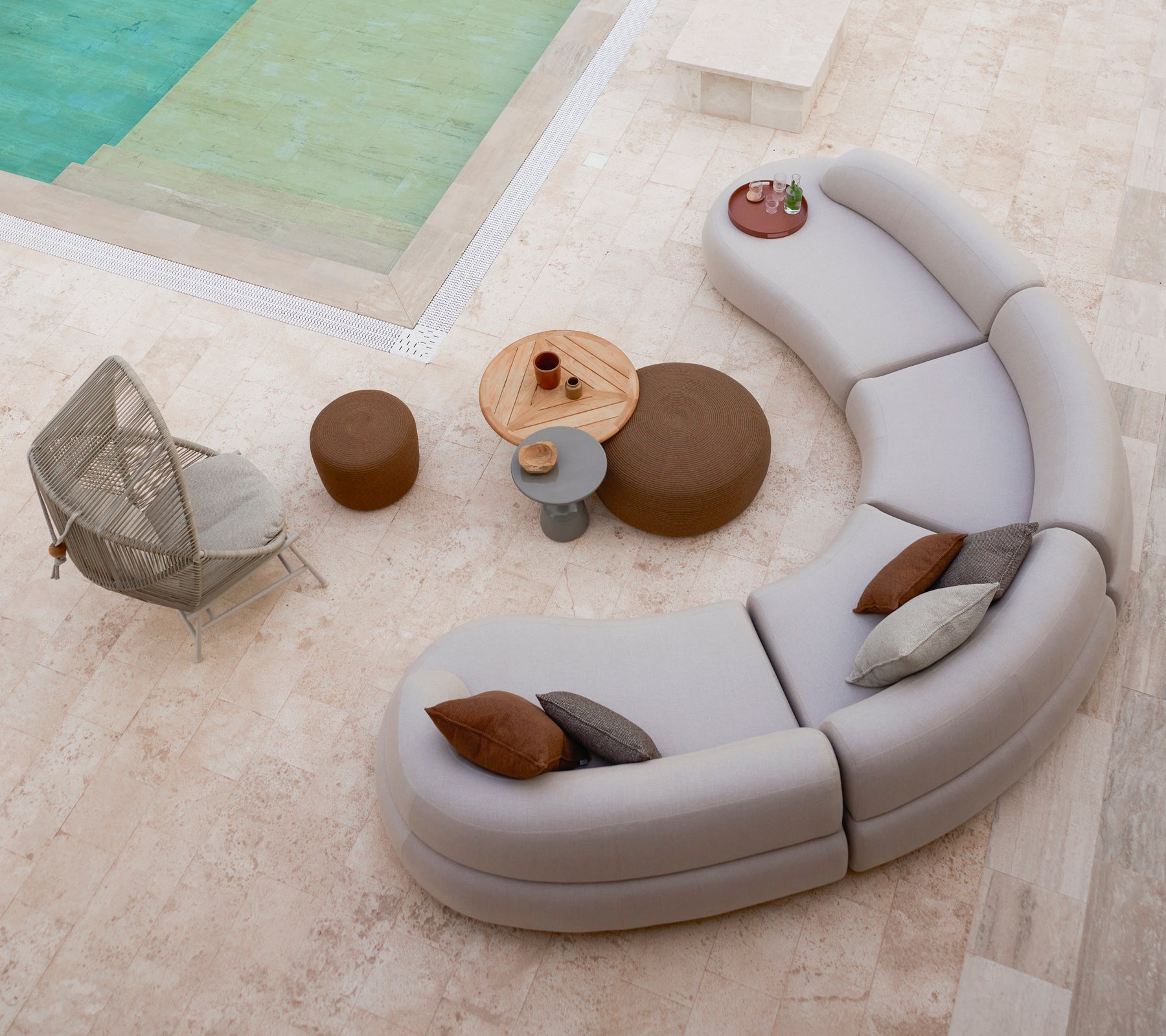 Curved lounge seating arranged with small and large circular footstools, alongside a Hive chair and a round table in a stylish setting.