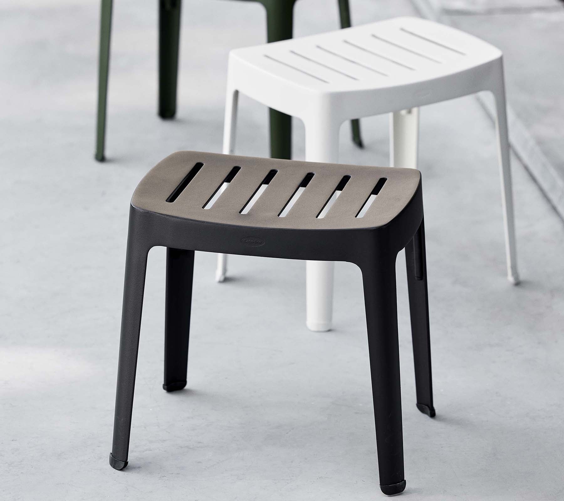Stylish cut stool in black with slatted top, featuring a modern design; complemented by a white stool in the background.