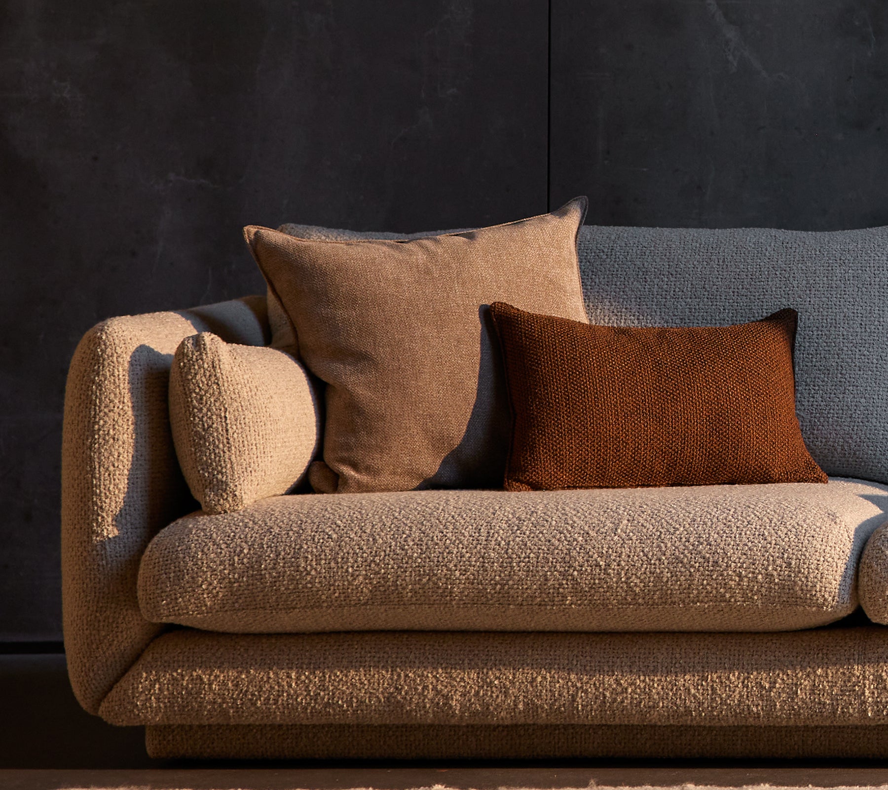 Essence and Rise scatter cushions placed on a textured Bloom sofa, featuring neutral tones against a dark background.
