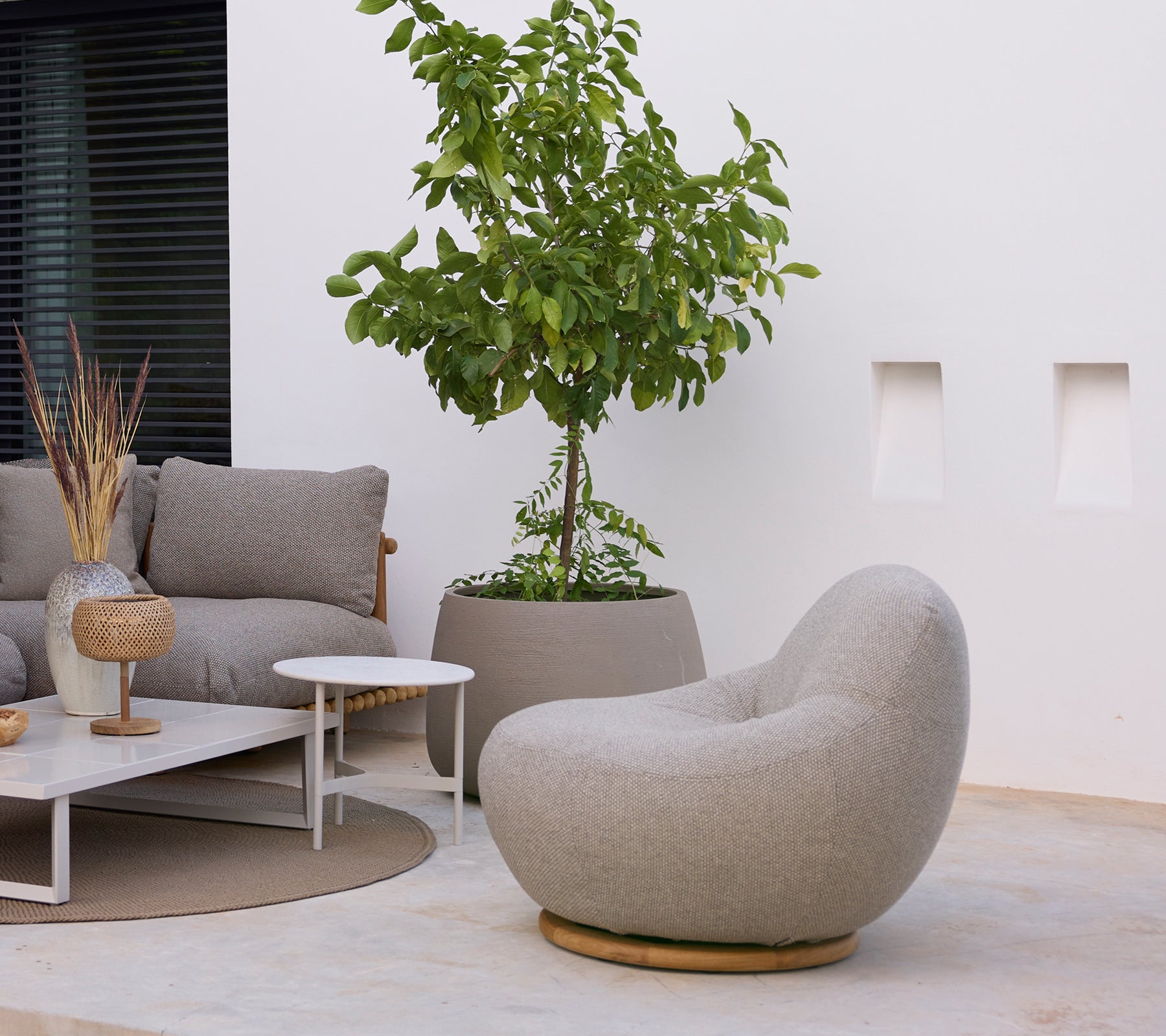 Modern lounge area featuring a grey chair, sofa, white coffee table, and green plant.