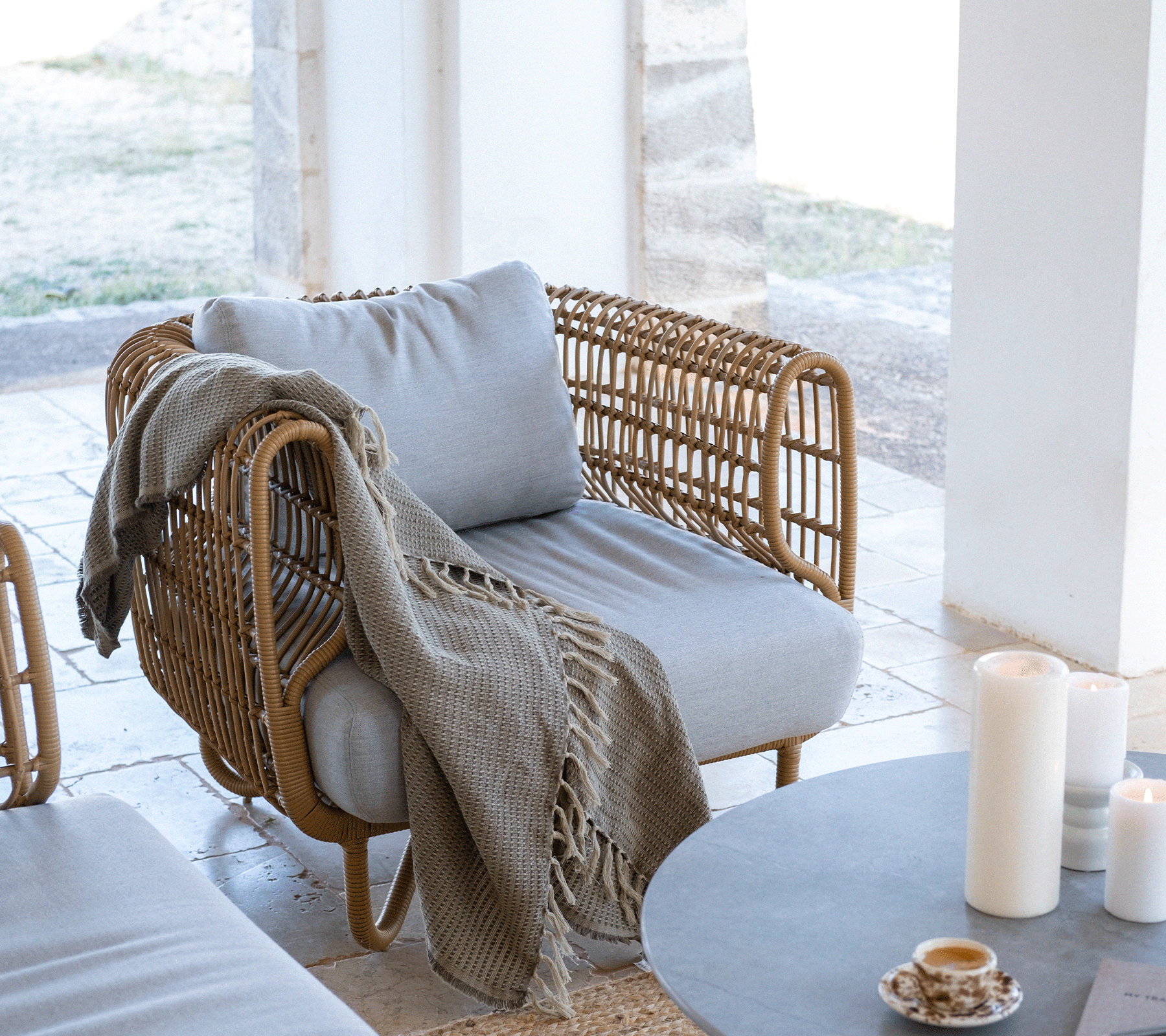 Cozy modern chair with light gray cushion, a knitted throw draped over the side, surrounded by candles and a minimalist table setting.