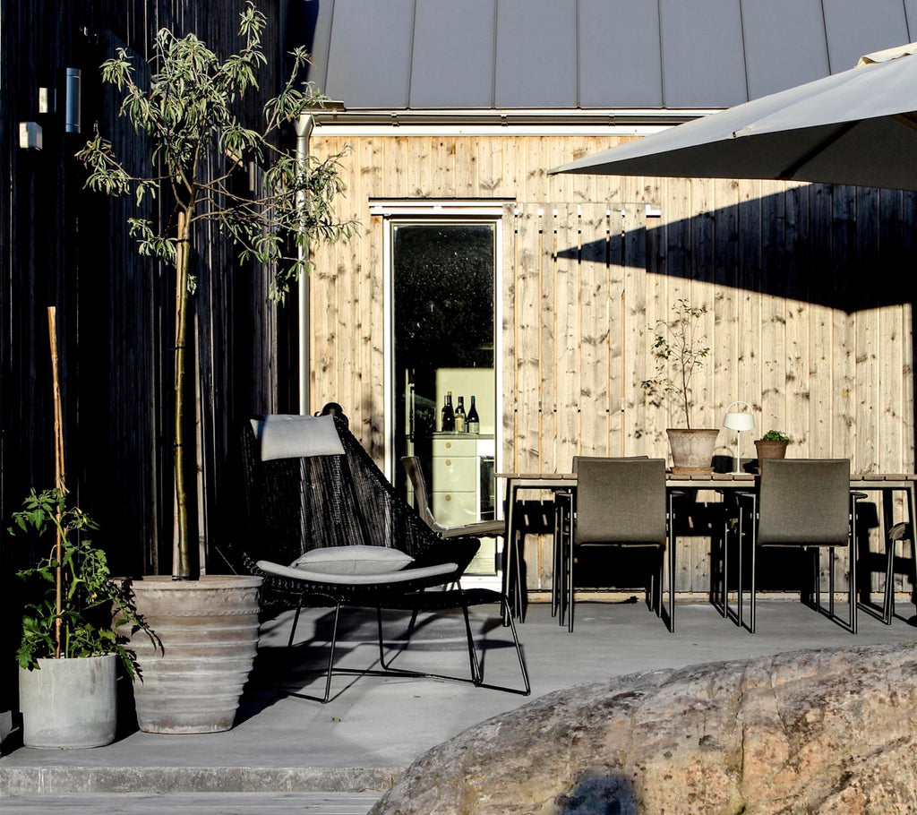 Outdoor lounge area featuring a black chair, grey table, and a potted plant.
