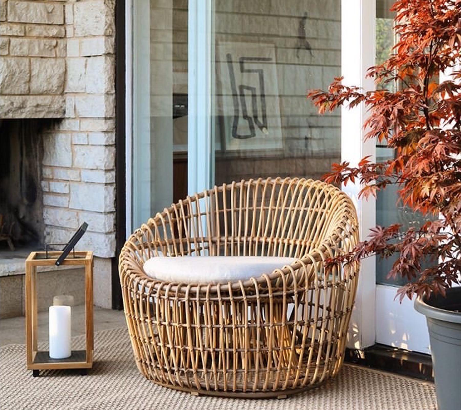 A stylish wicker chair with a cushion, accompanied by a lantern and a vibrant plant, enhancing a cozy, inviting space.