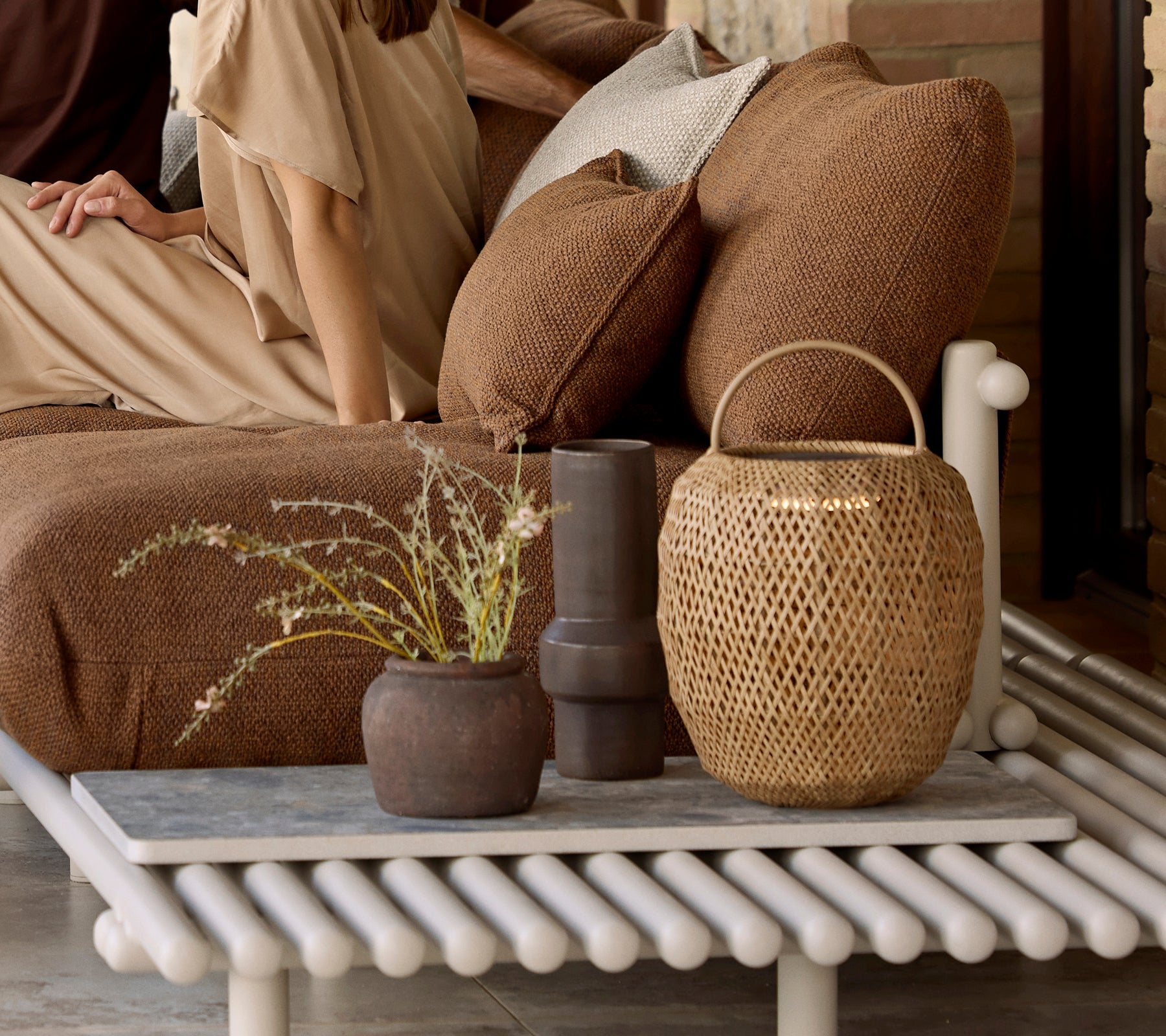 A decorative arrangement featuring a glow lamp, textured cushions, and various vases on a unique, slatted table.