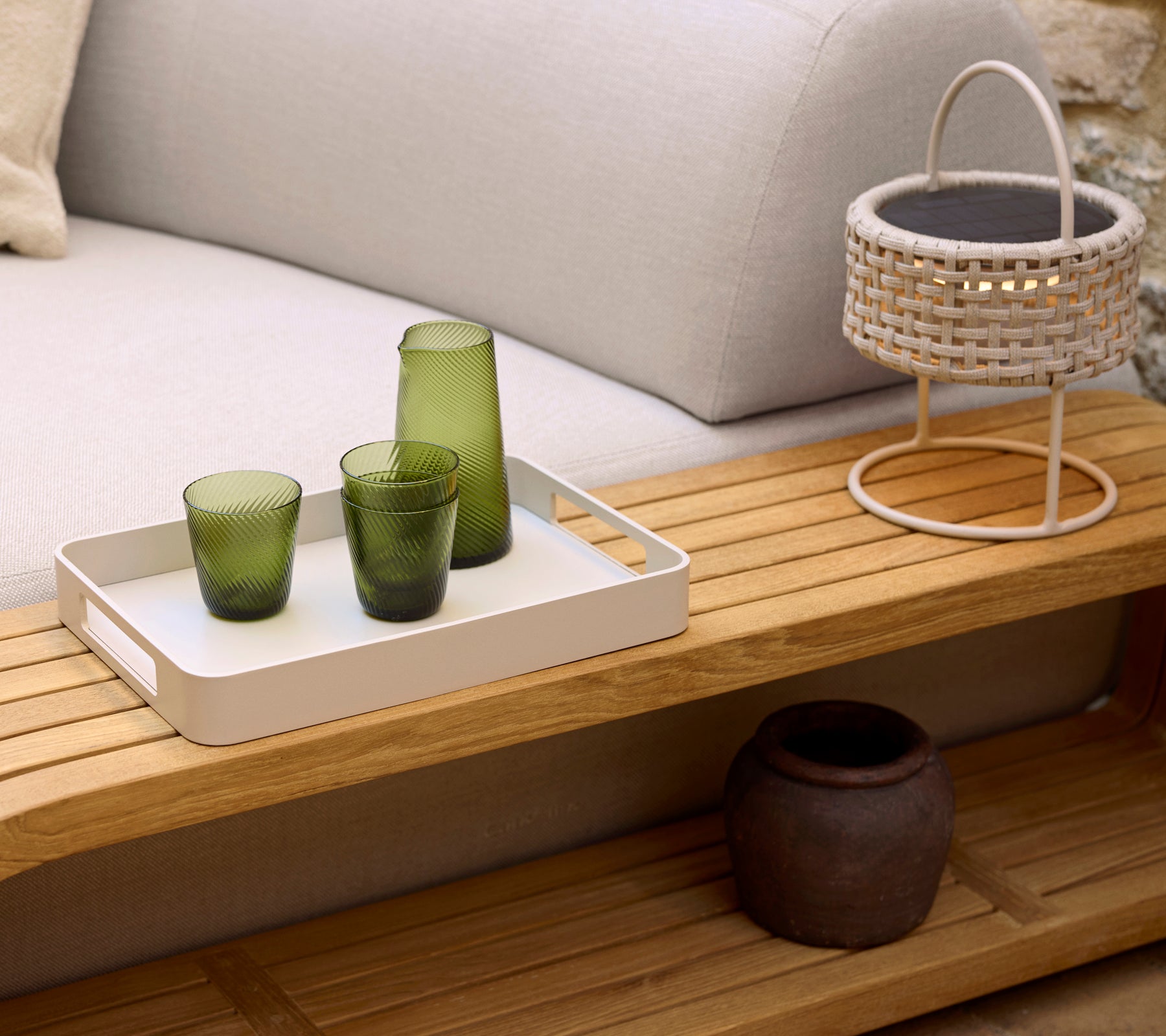 A cozy coffee table featuring a white tray with three green glasses, a woven lamp, and a decorative pot, enhancing a serene ambiance.