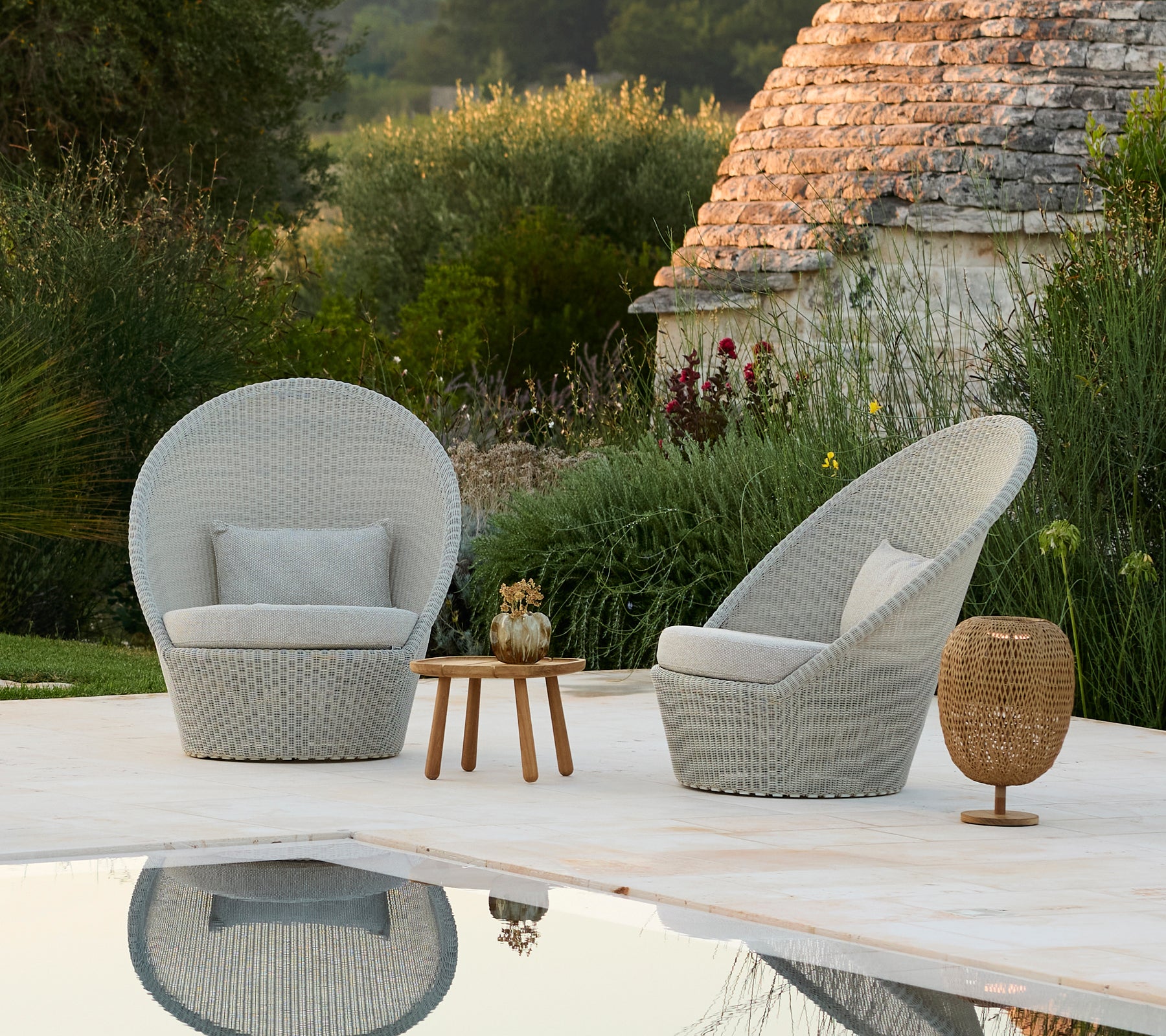 Two grey lounge chairs and a wooden side table beside a pool in a modern outdoor setting.