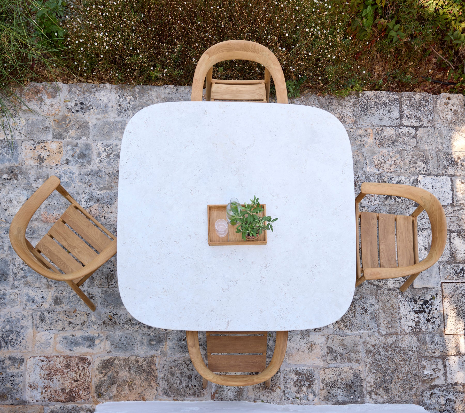 Modern white table with wooden chairs and a small plant centerpiece in an outdoor setting.