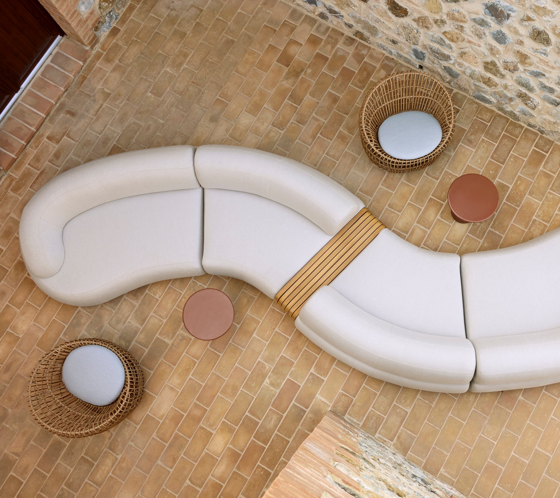 Mellow lounge with a curved white seating arrangement, two round Glaze coffee tables, and woven Nest chairs on a stone floor.