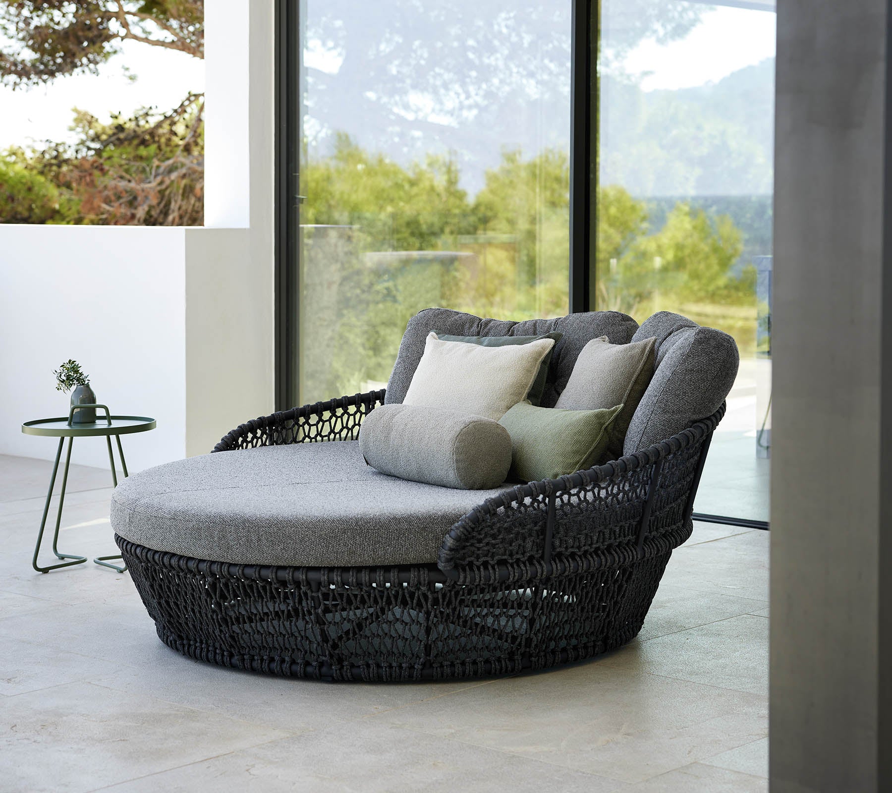 Stylish ocean daybed with gray cushions, surrounded by large windows showcasing a scenic outdoor view.