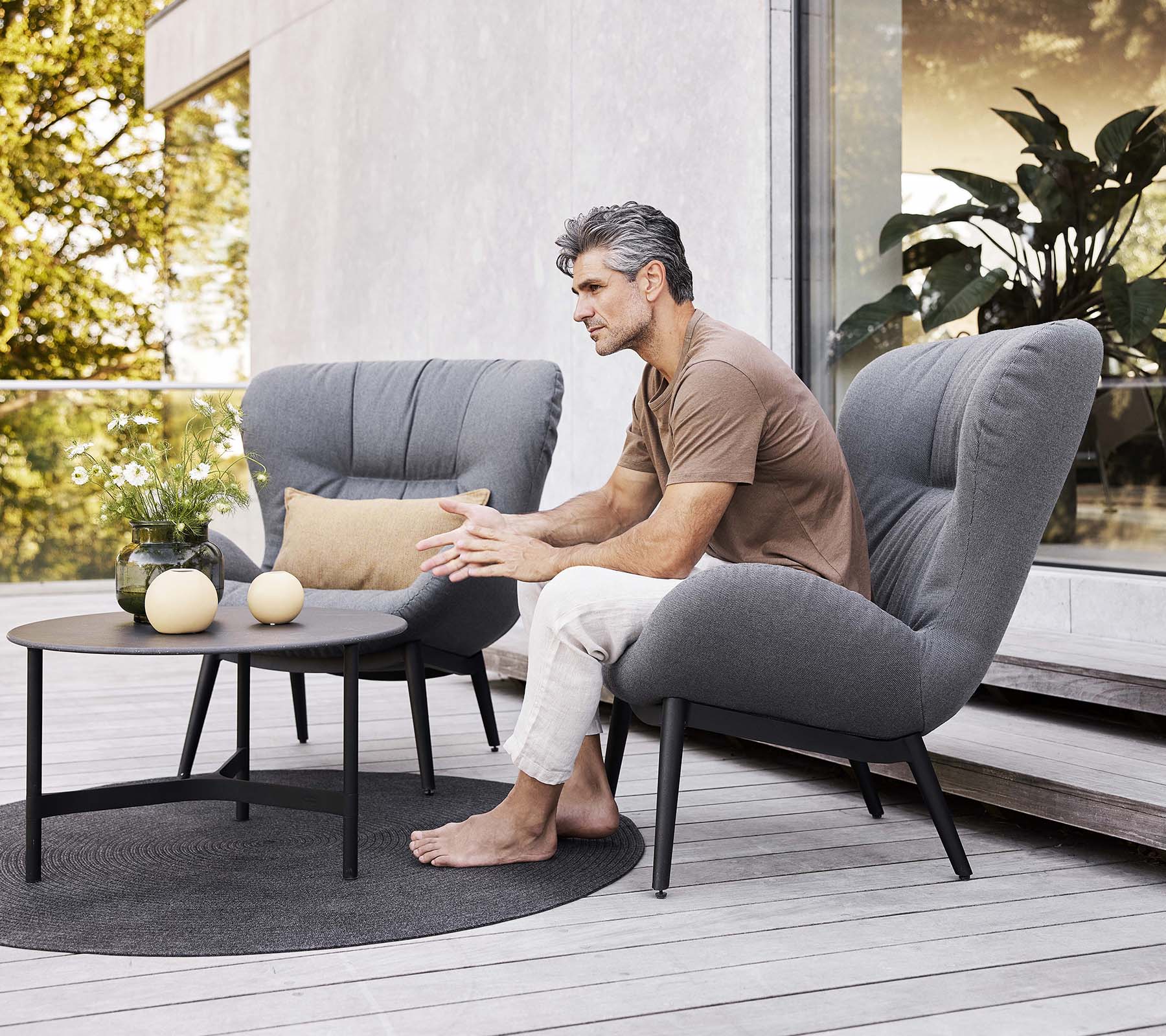 A serene lounge chair set with a man seated, a small table nearby, and decorative items, creating a relaxed atmosphere.