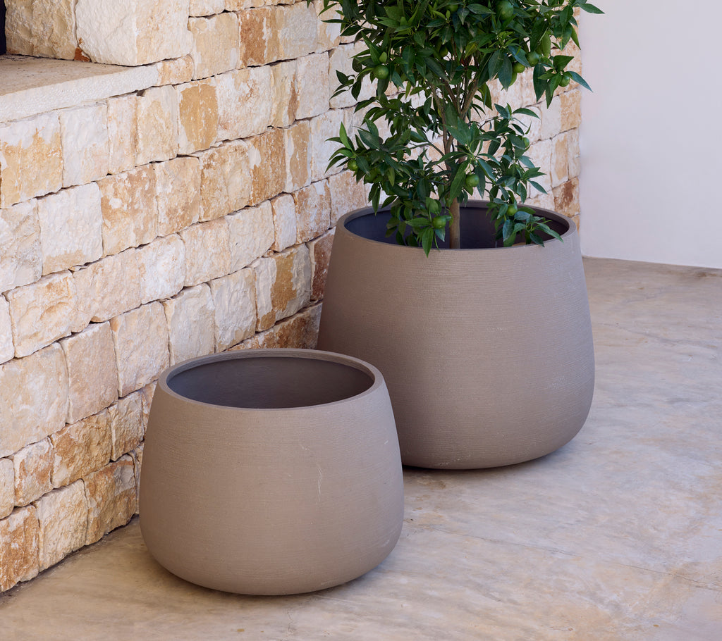 Two modern grey planters with a green plant set against a stone wall.