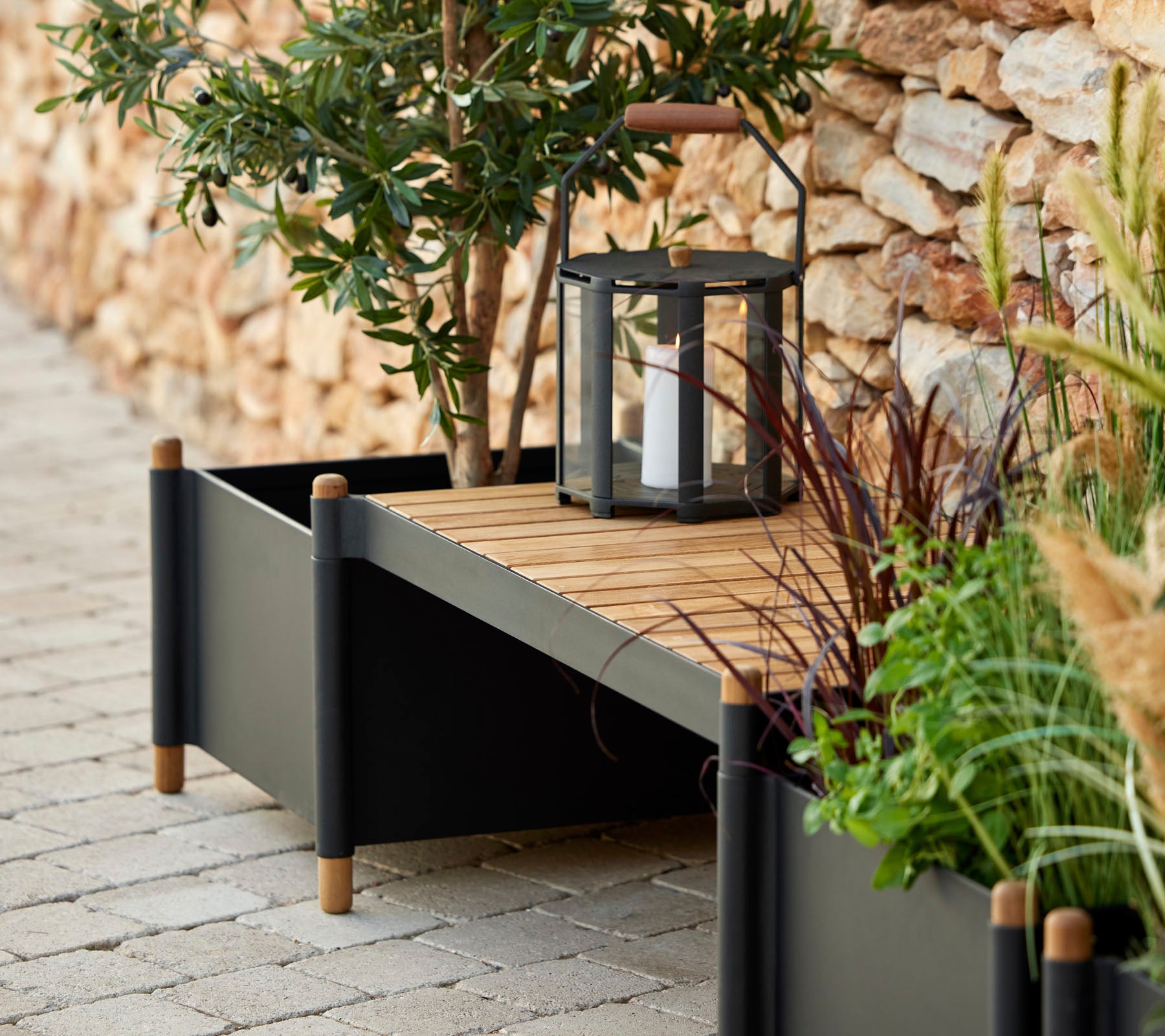 A stylish planter box with wooden slats, surrounded by greenery and a lantern, adding a touch of elegance to the space.