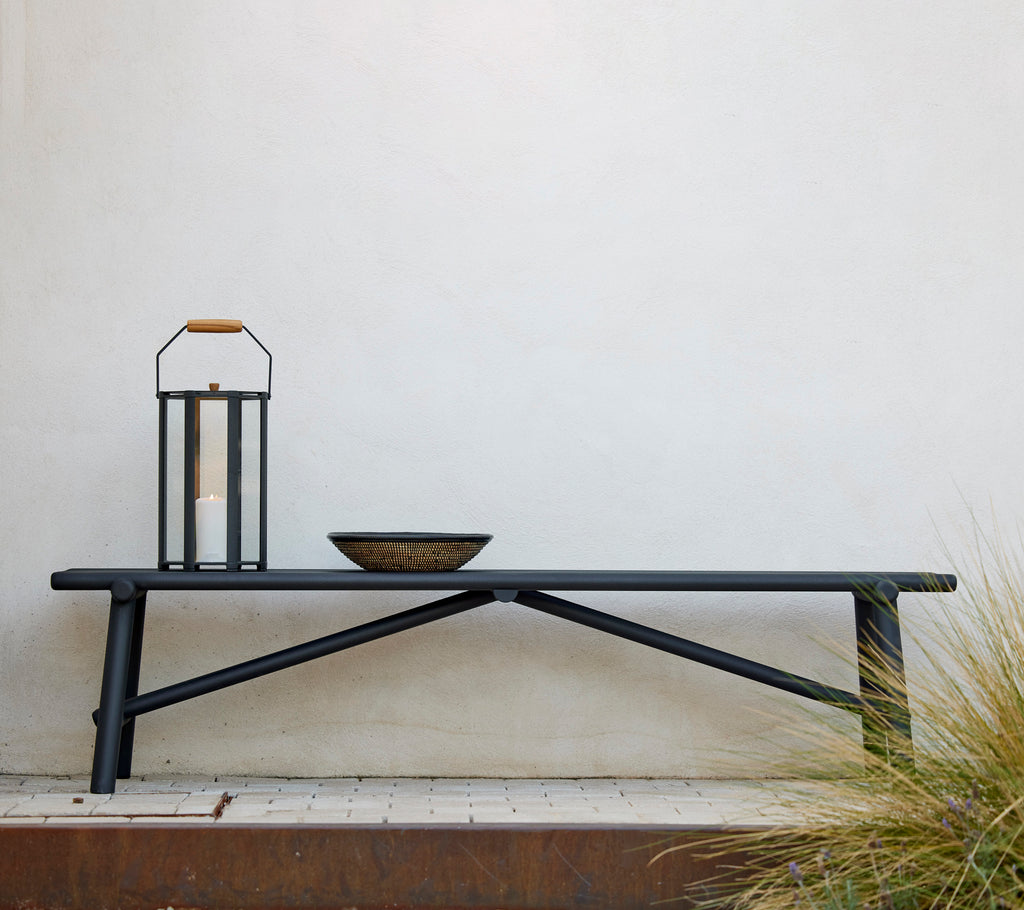 Aluminium bench in lava grey with a decorative bowl and lantern, set against a plain wall.