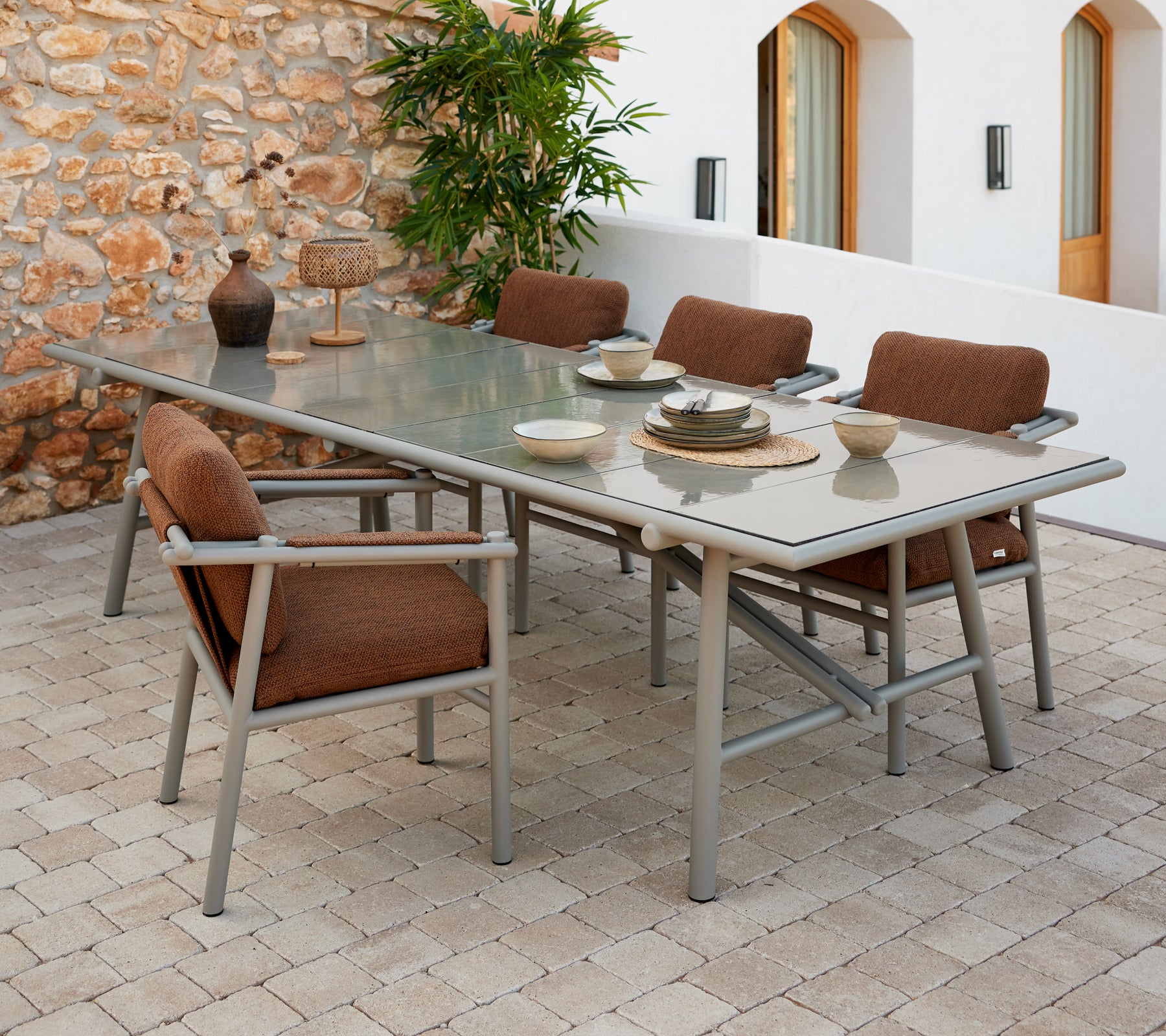 A spacious dining table set featuring aluminum sticks, with brown cushioned chairs and tableware arranged on a glass surface.