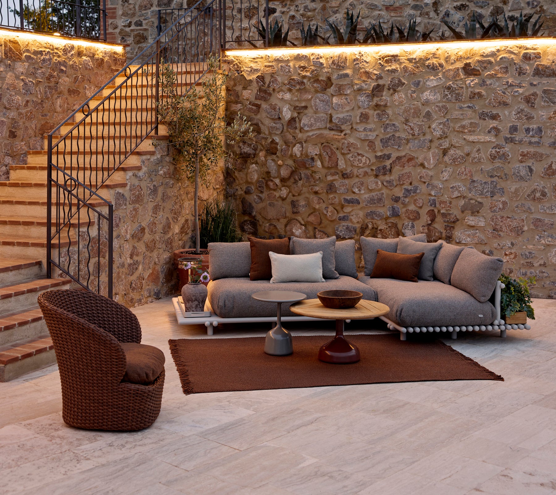Cozy seating area featuring a modular sofa with cushions, a round coffee table, a knit rug, and a woven lounge chair.