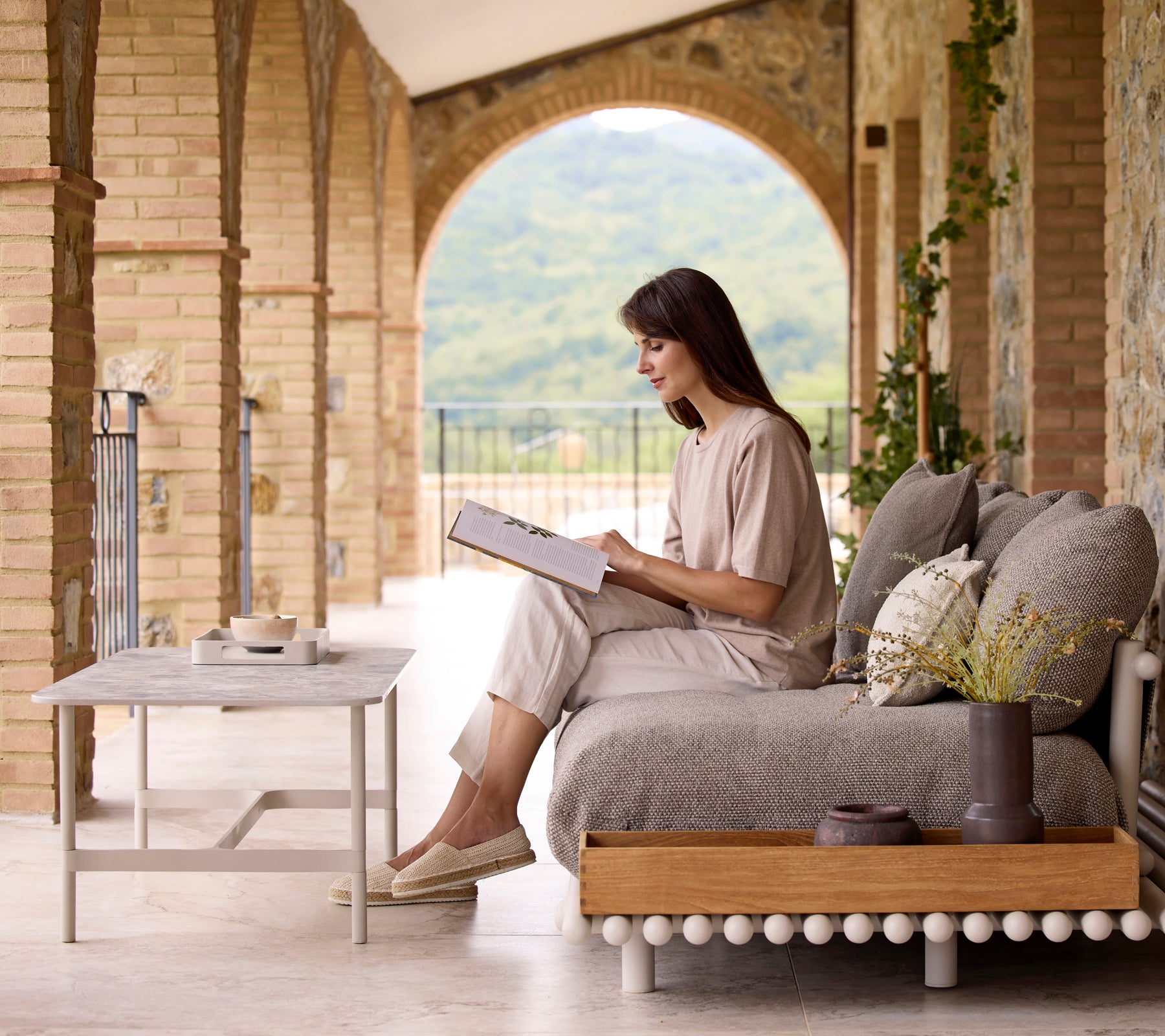 A woman sits comfortably, reading a book beside a Twist rekt coffee table with a stylish club storage box, surrounded by natural elements.