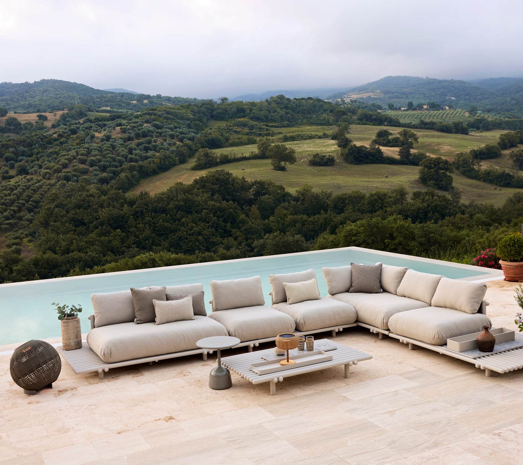 Aluminium lounge seating on a platform, featuring neutral cushions and an Illusion round lamp, set against a scenic landscape.