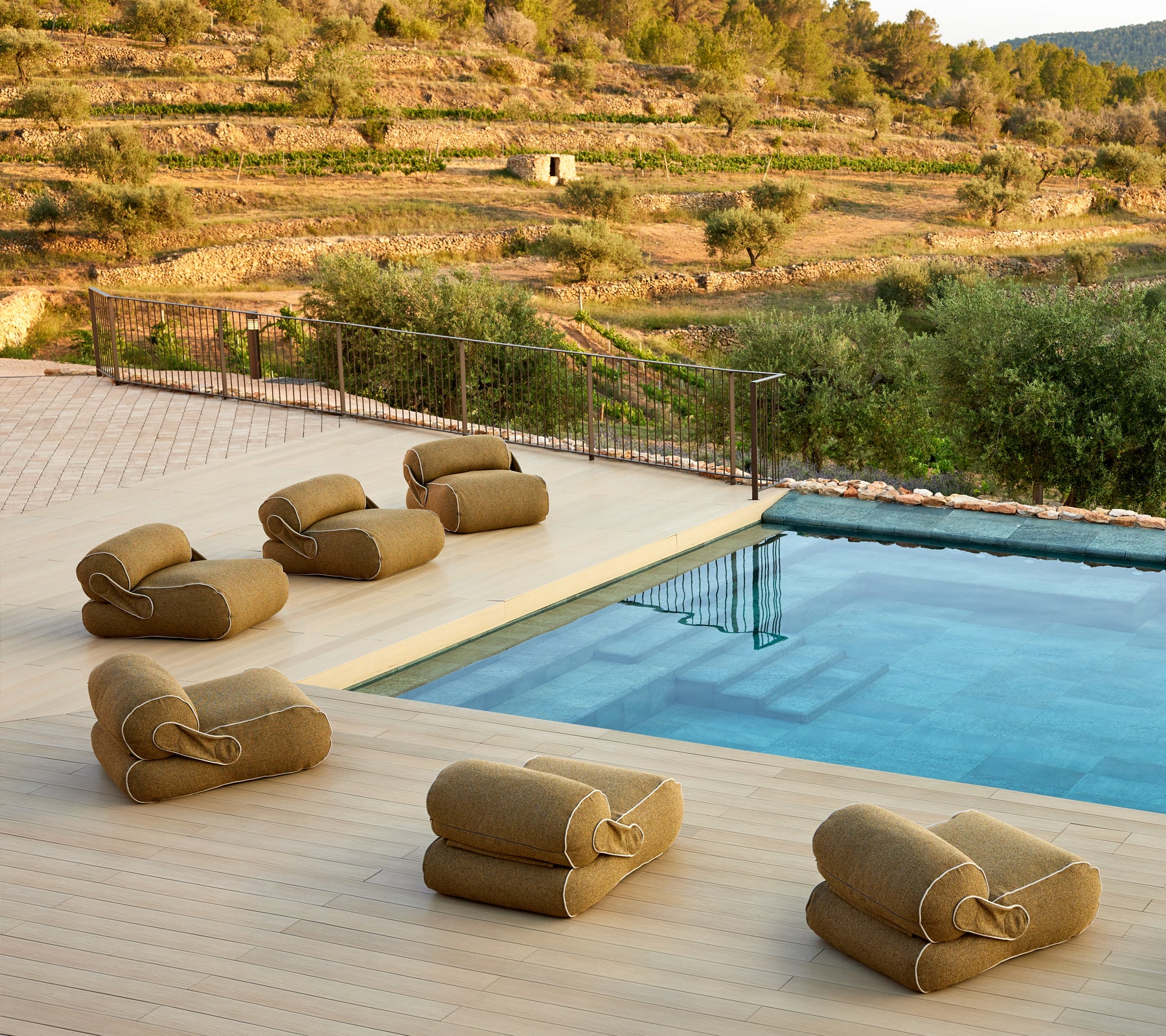 A serene setting featuring cushioned lounge seating arranged near a tranquil pool, surrounded by lush greenery and a scenic landscape.