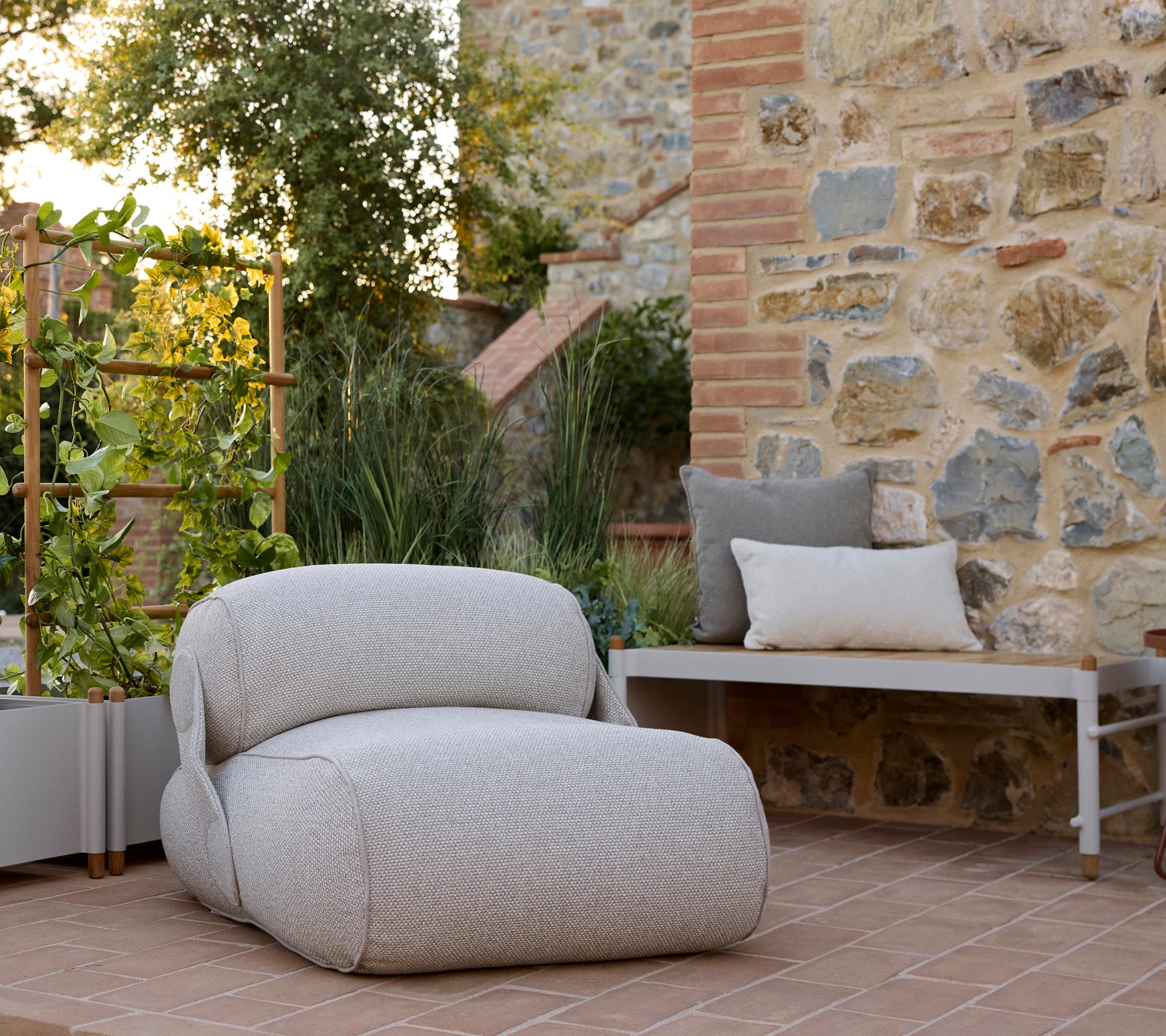 A cozy lounge chair with a textured fabric, accompanied by a sleek planter bench and lush greenery in a serene setting.