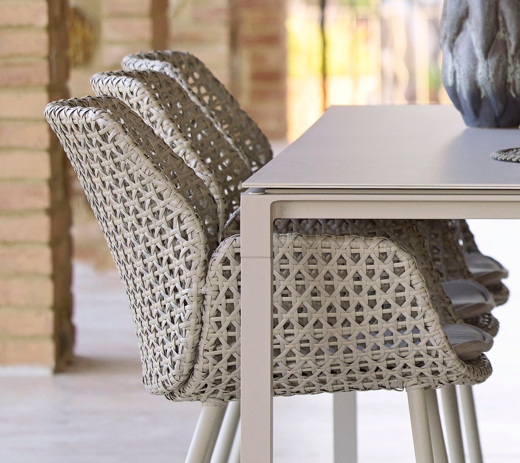 Stacked chairs with a unique woven design beside a smooth, minimalist dining table, creating a modern and inviting dining arrangement.