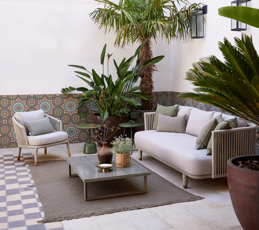 Cozy lounge area featuring a light sofa, potted plants, decorative table, and textured flooring, creating a serene ambiance.