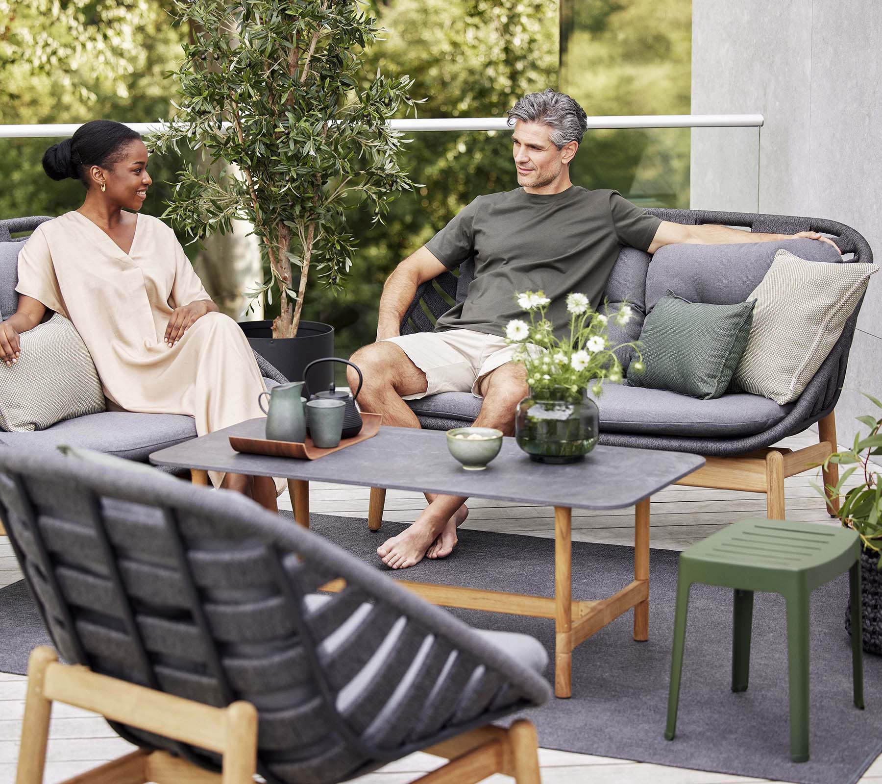 A cozy seating arrangement with a couple enjoying conversation, surrounded by greenery, featuring soft cushions and a stylish coffee table.